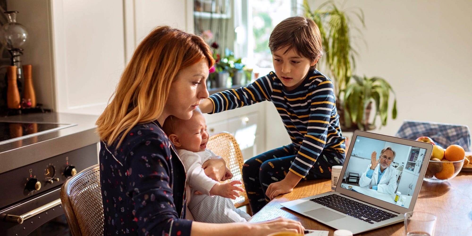 A woman and her two children sit at the counter looking at a computer for a telehealth appointment.