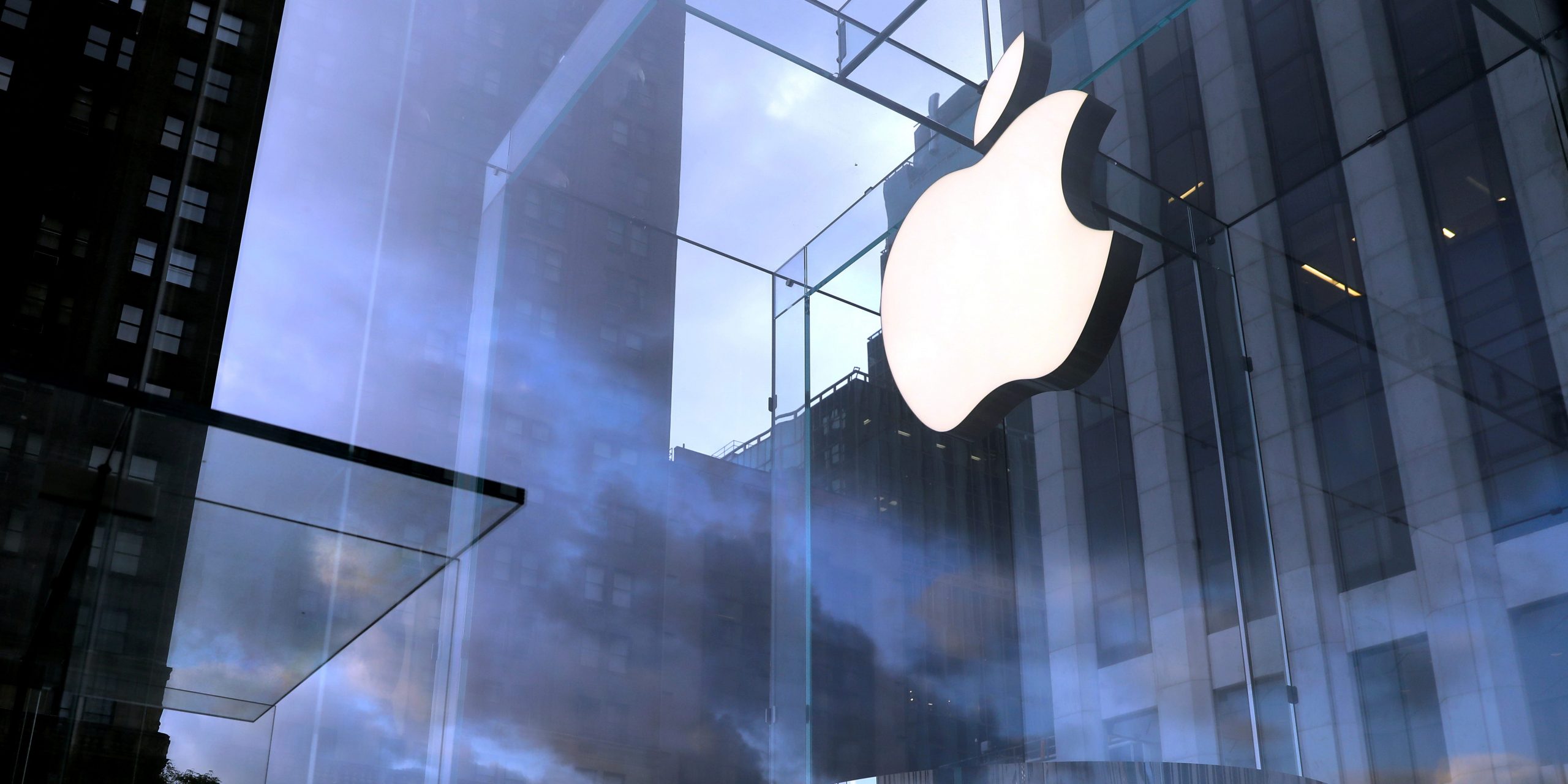 A cloudy sky behind a brightly lit Apple logo in a Manhattan store