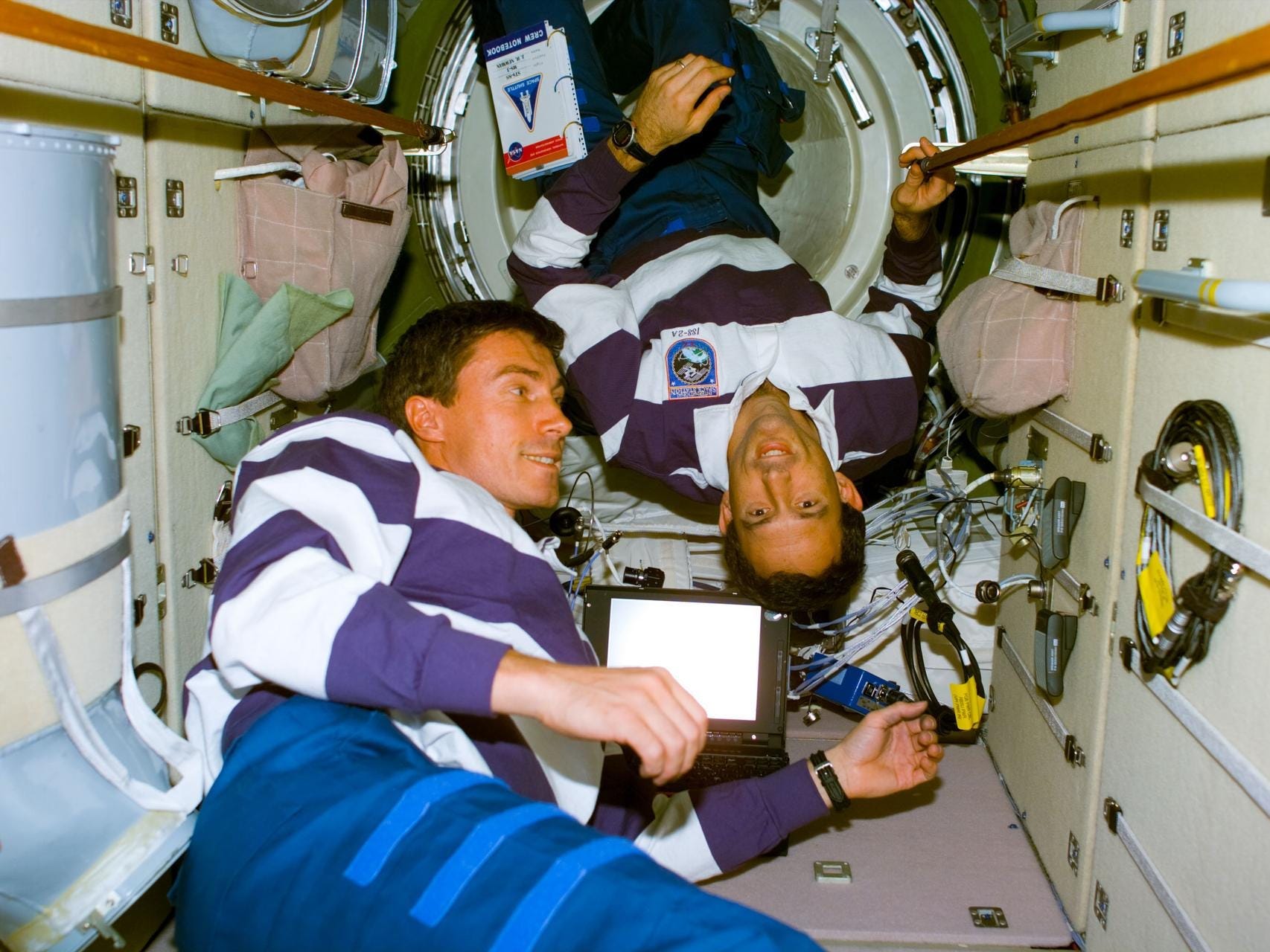 1990s astronauts in striped shirts inside cramped hallway of zarya space station module