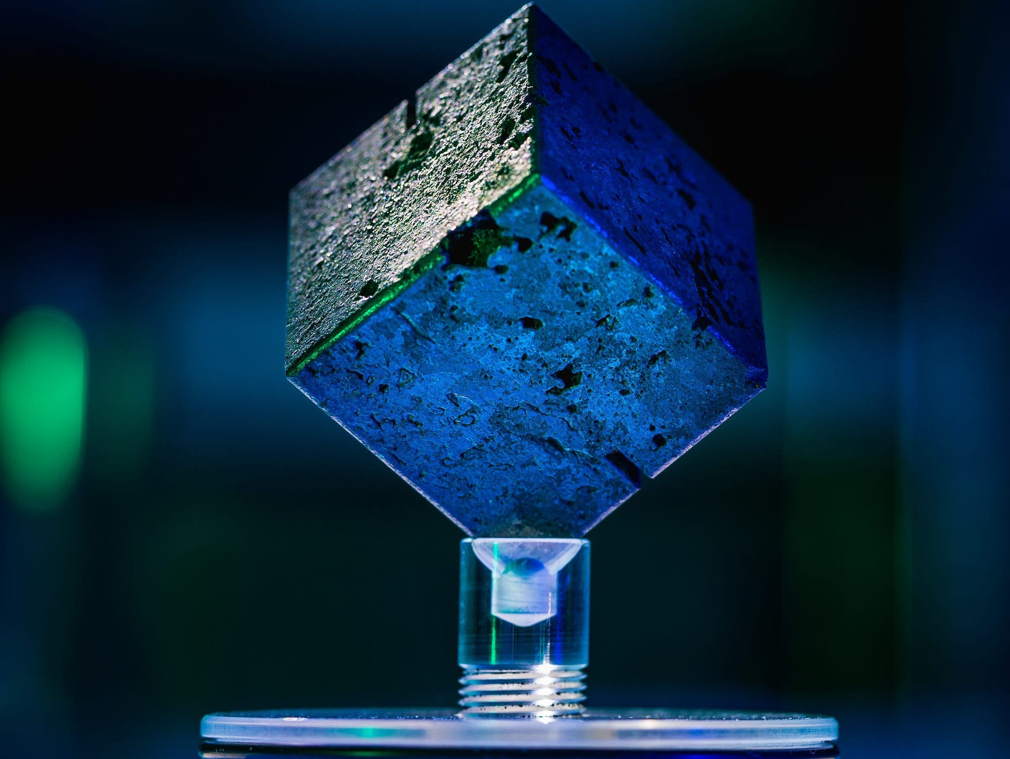 a grey cube is balanced on a vertex on a plastic display.