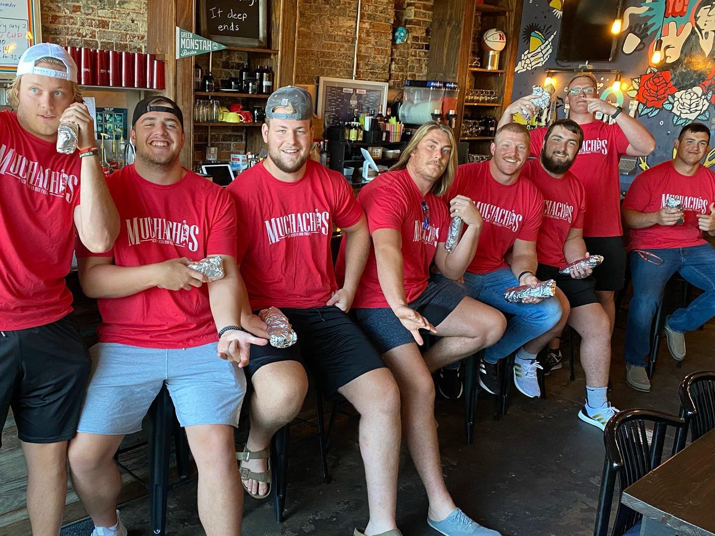 The offensive lineman of the University of Nebraska pose with burritos wearing red shirts at Muchachos.