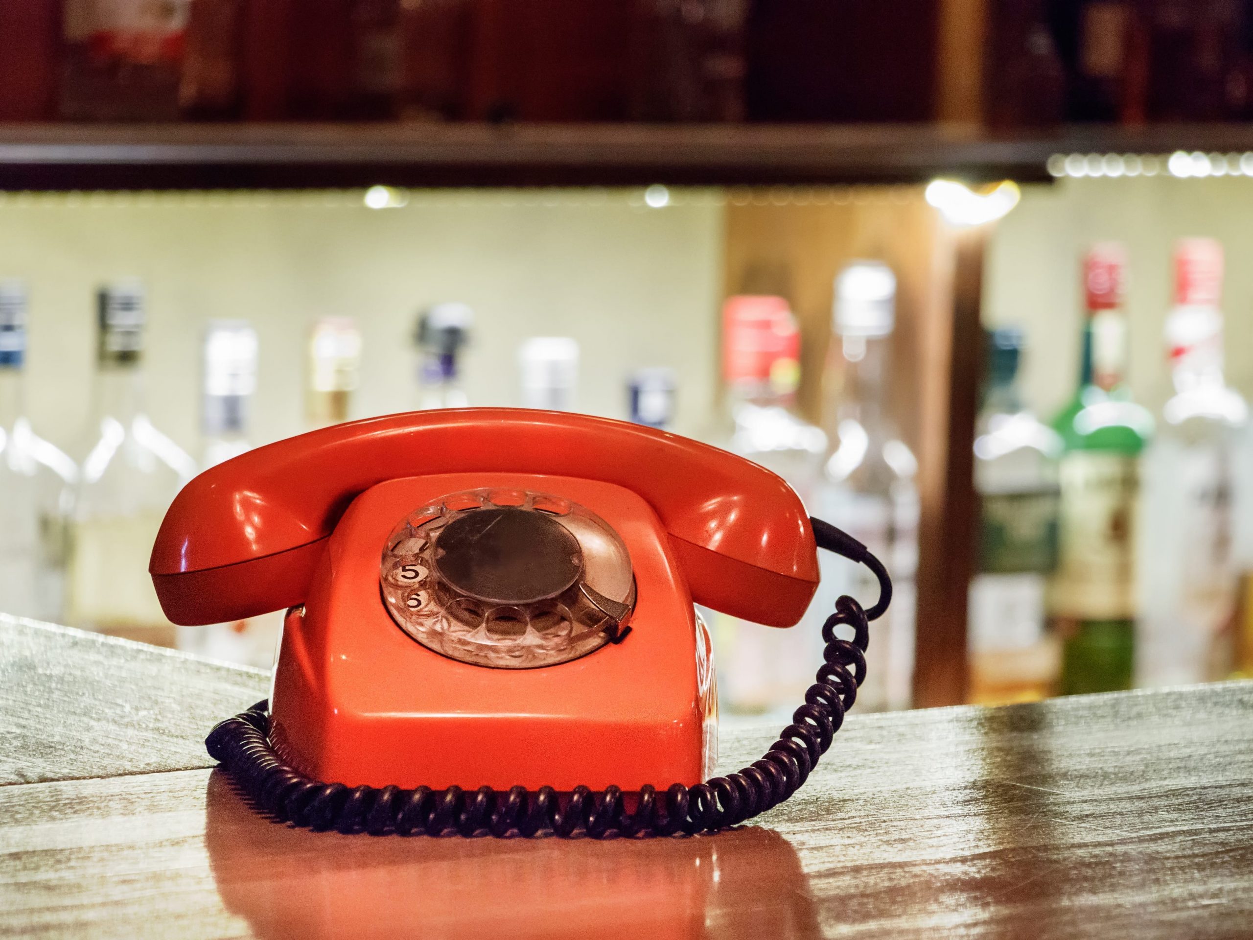 A vintage plastic orange telephone with dial placed on a wooden table inside a bar.