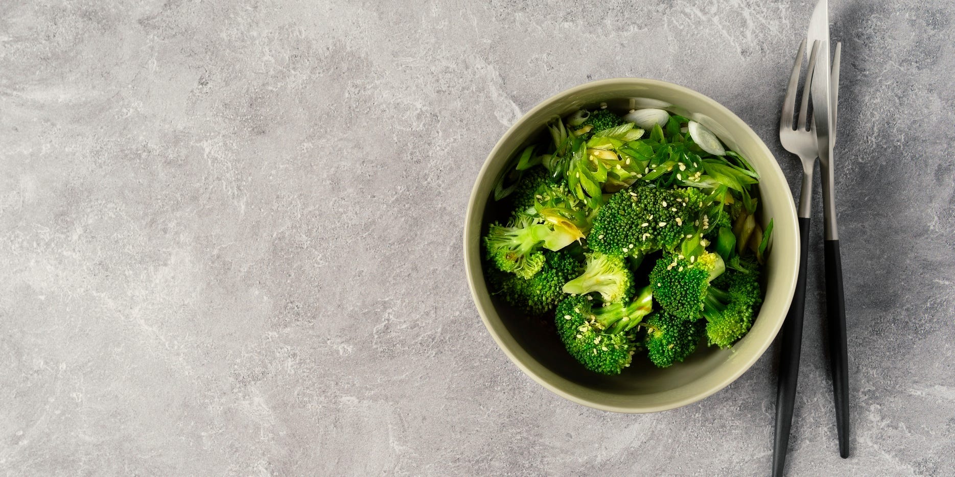 A bowl of steamed broccoli against a gray background.