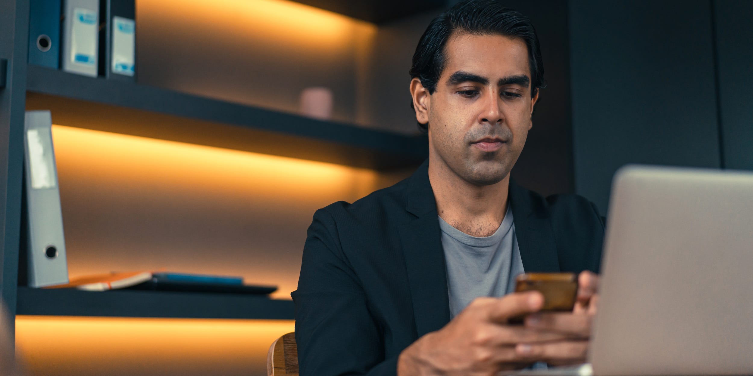 business professional in office looking at phone and laptop