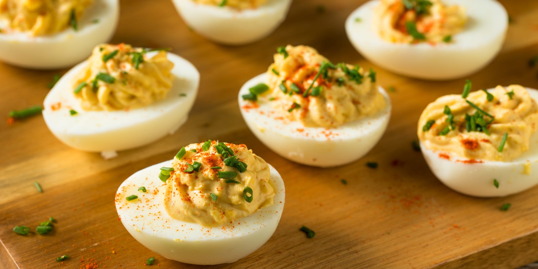 Deviled eggs topped with paprika and chives on a wooden cutting board