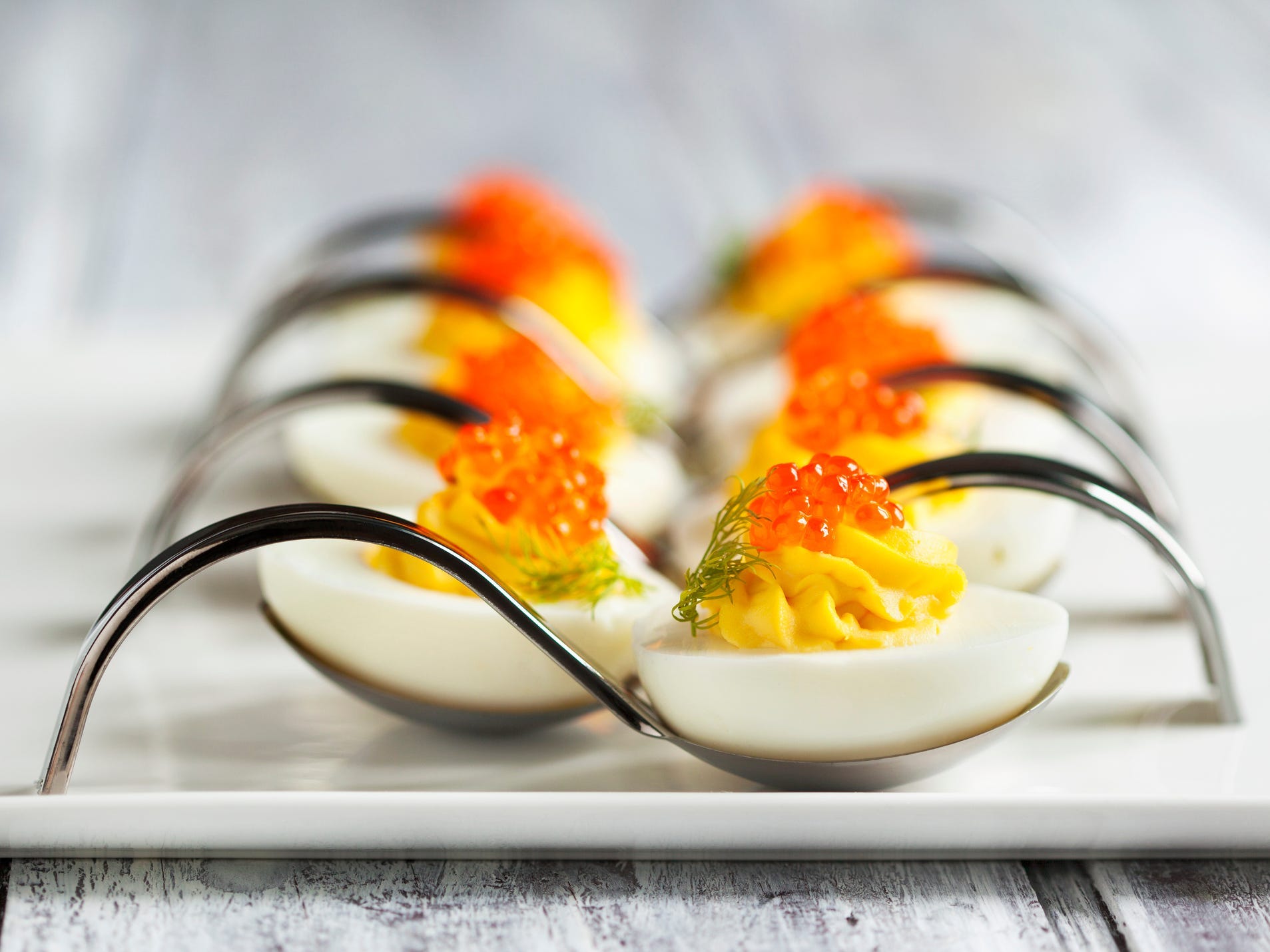 Deviled egg halves topped with salmon roe sitting in individual silver serving spoons