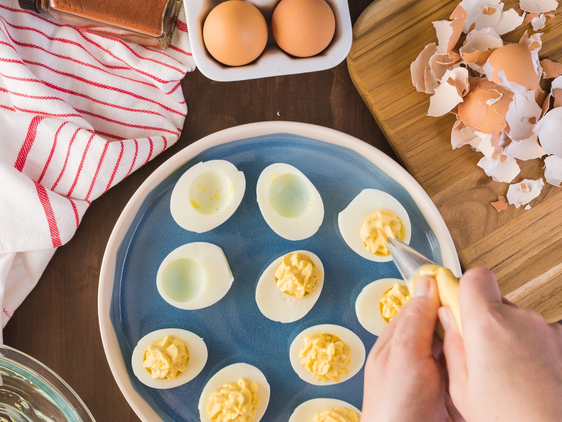 A pair of hands piping egg yolk filling into hard-boiled egg whites to make deviled eggs