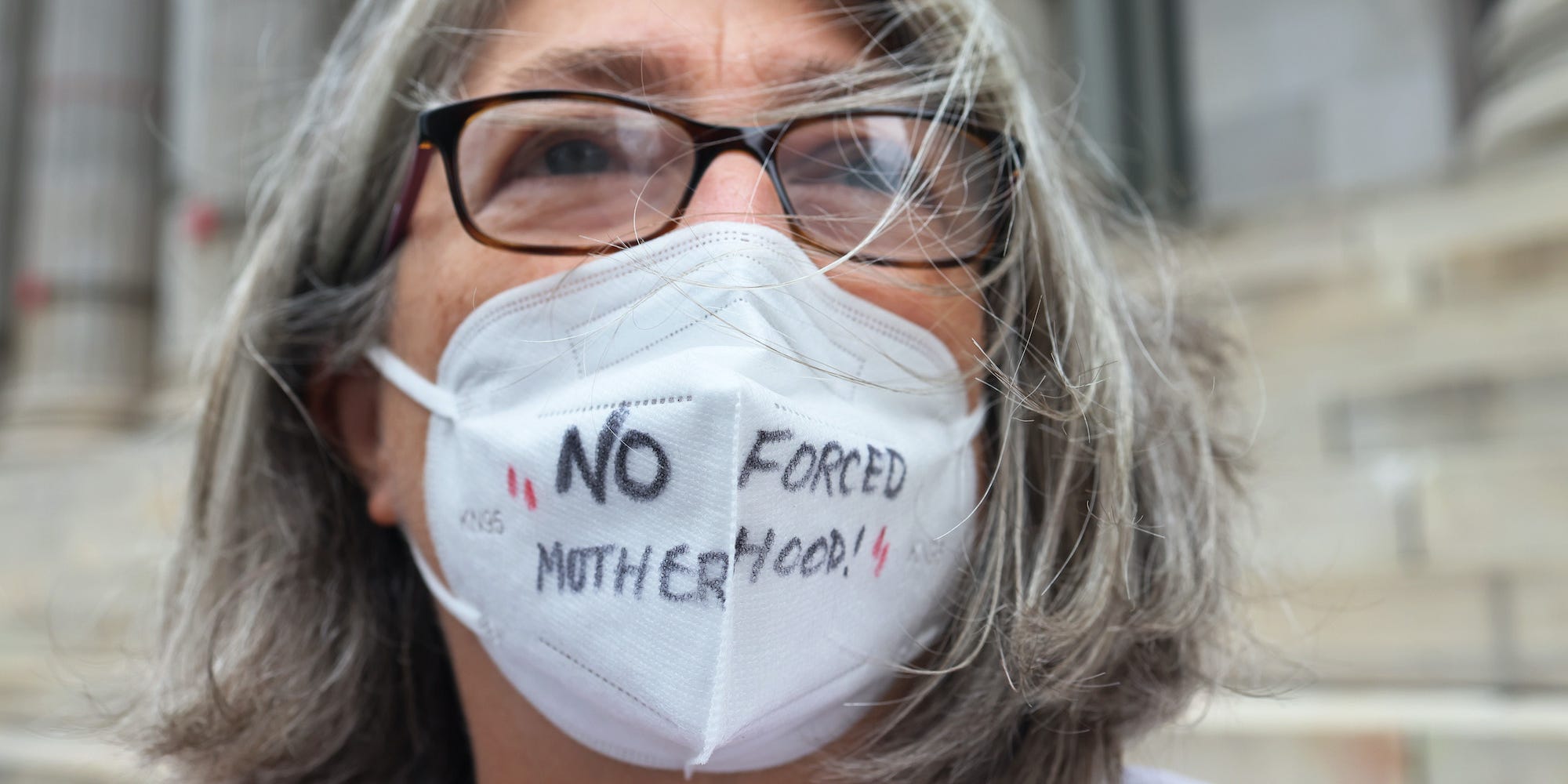 A woman wears a mask that says 'No forced motherhood'