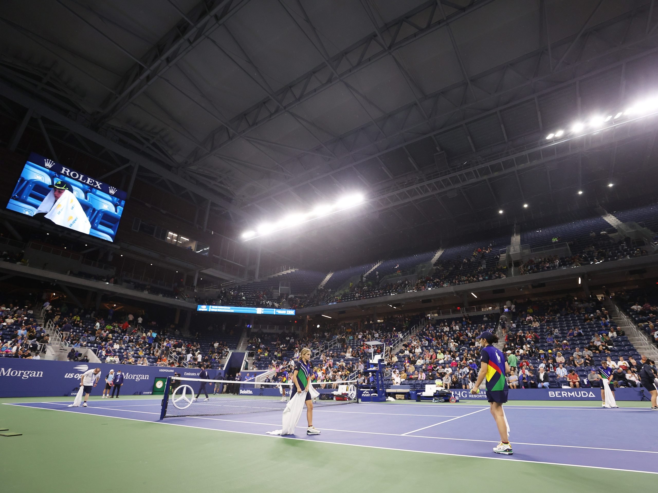 Crew members dry the court after rain enters through the outer openings of the roof