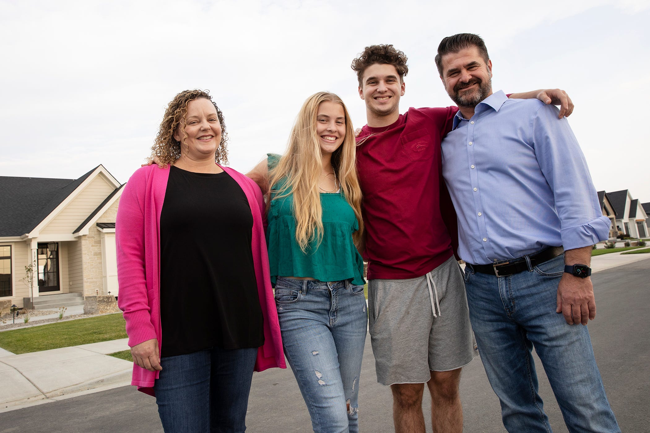 The Jansezian family stand on their street in front of their new house smiling with their arms around each other.