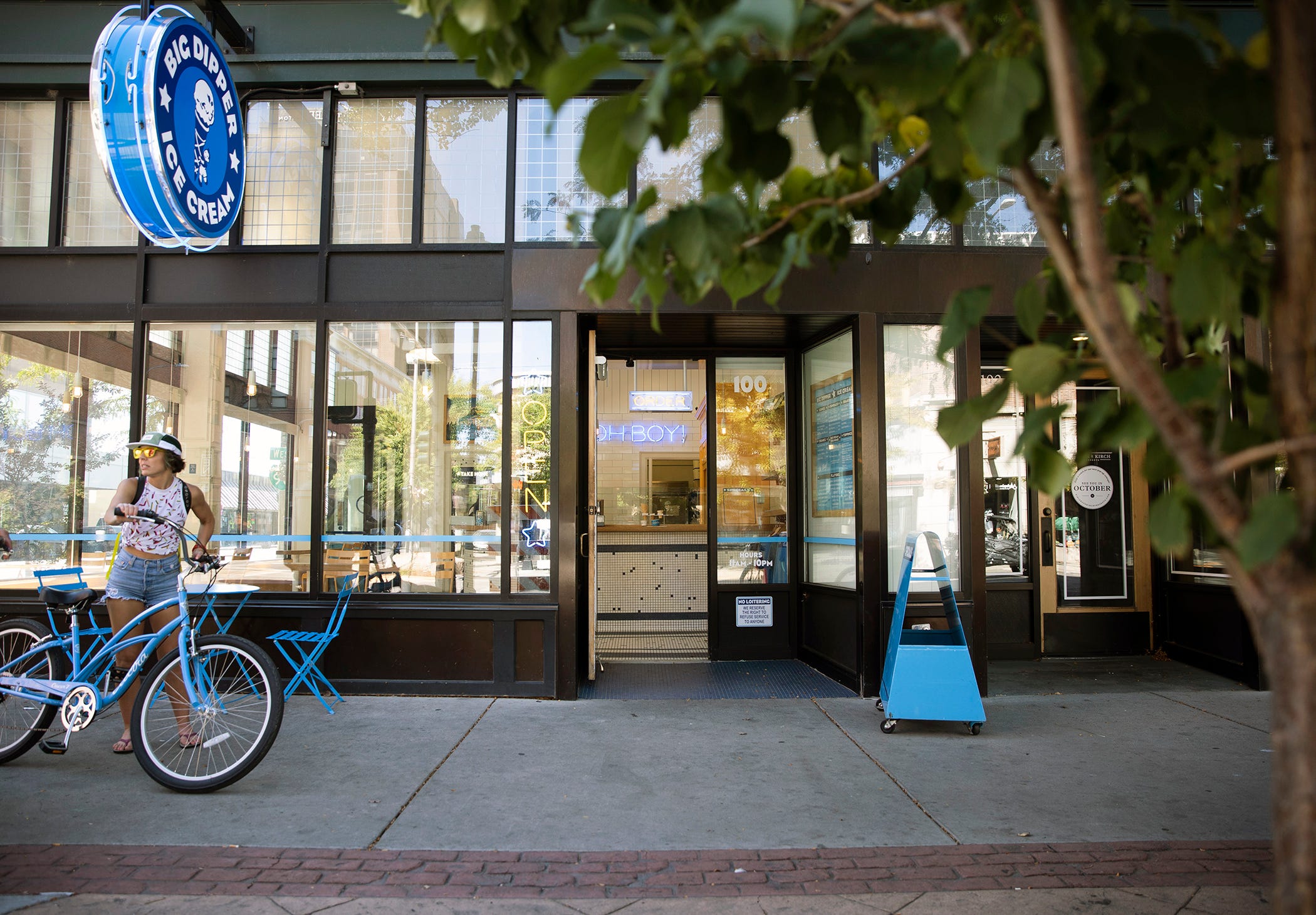 A woman holds her bright blue bicycle outside the glass-walled front of the Big Dipper Ice Cream in Billings, Montana.