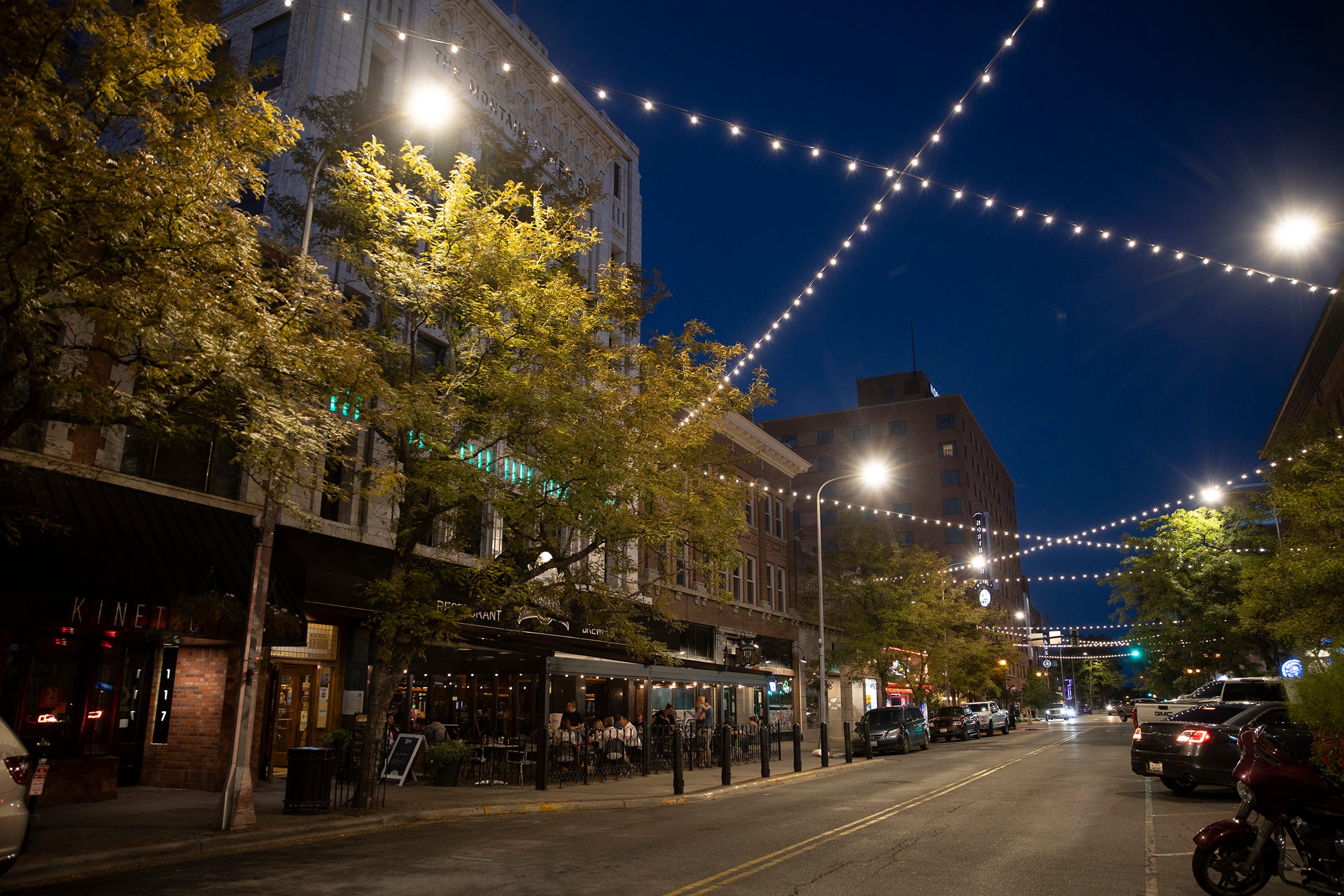 Fairy light are suspended above a wide road in downtown Billings at night.