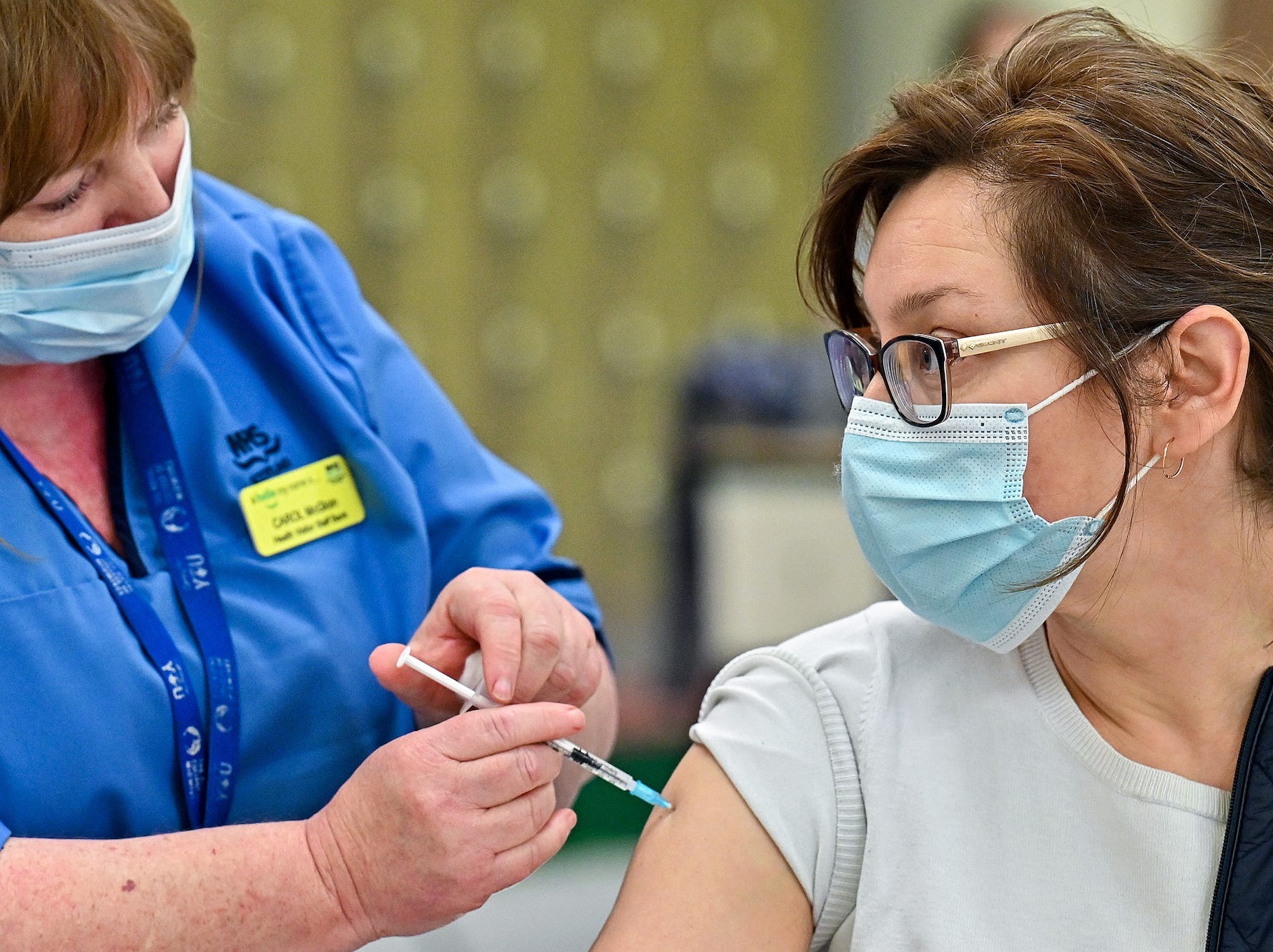 A health professionals gives a woman wearing a mask a COVID-19 vaccine in the arm in Scotland.