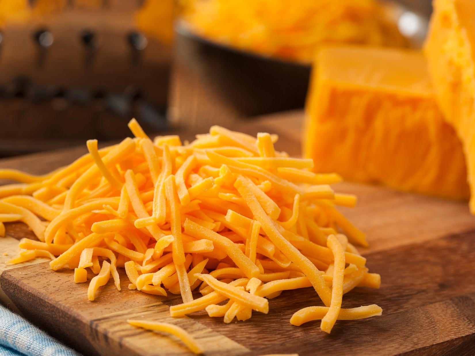 A pile of shredded cheddar cheese on a cutting board