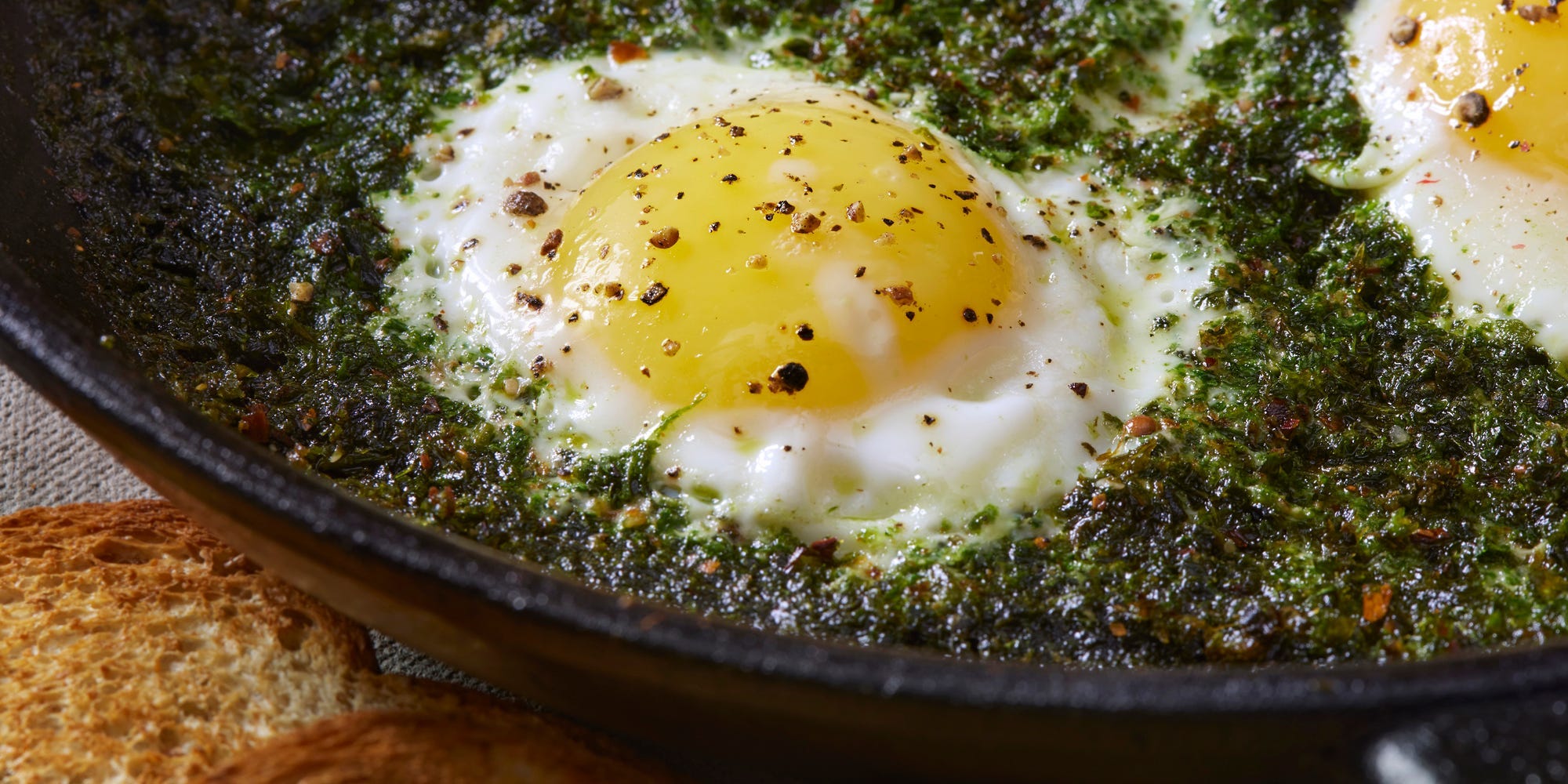 Three eggs surrounded by pesto in a pan.