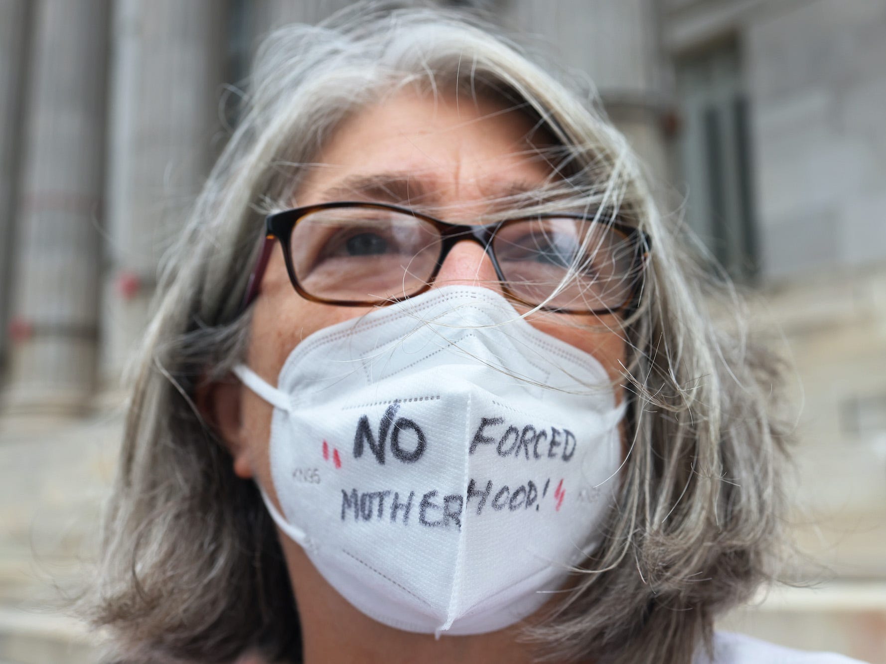 A woman wears a mask that says 'No forced motherhood'