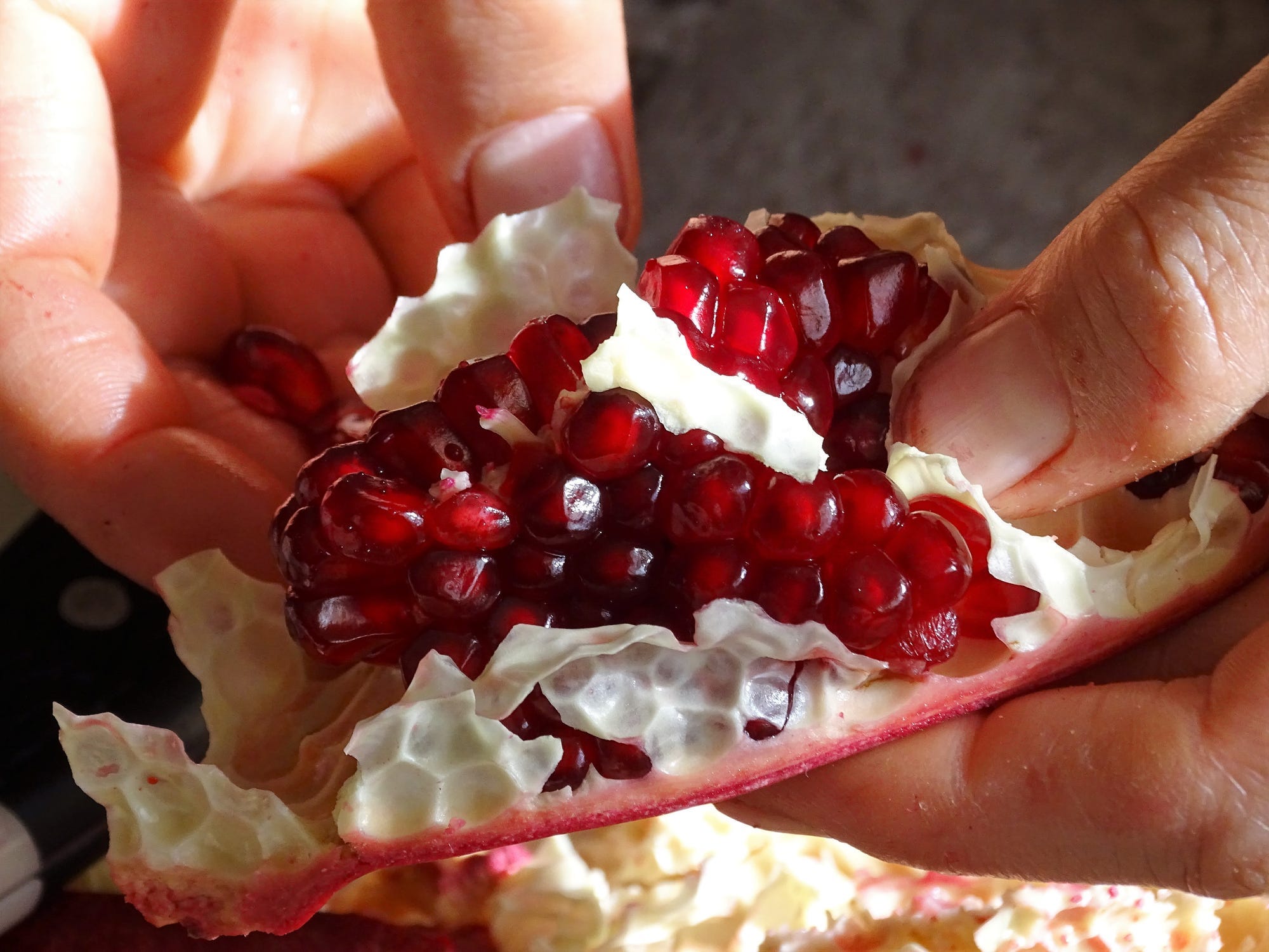 A closeup of a person's hand pulling the seeds out of a section of pomegranate