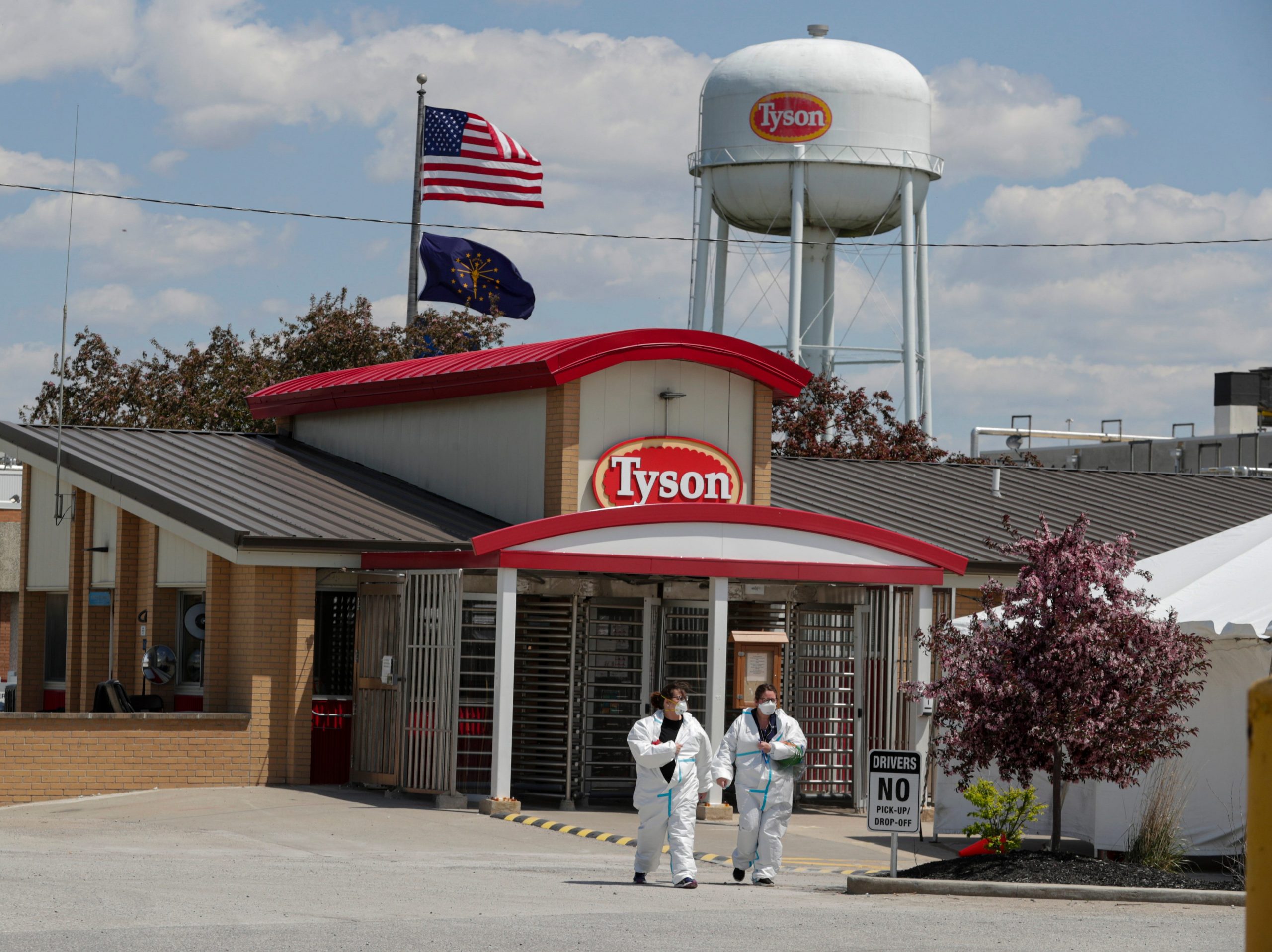 Two people wearing white jumpsuits leave a Tyson Foods facility on a sunny day in Indiana