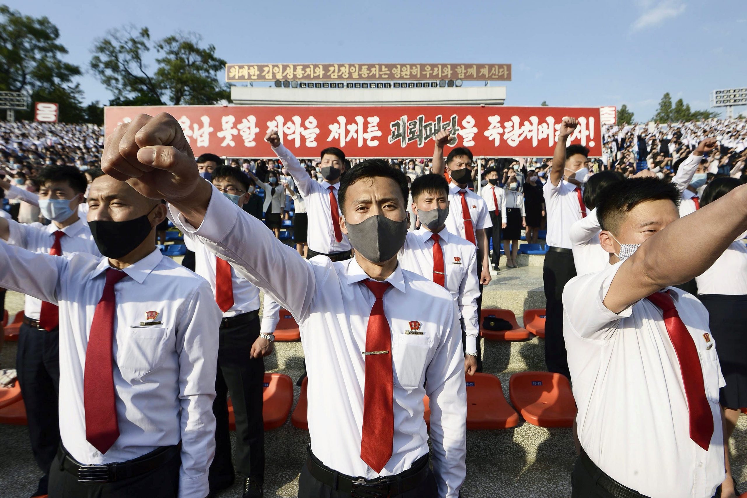 young people in north korea wear face masks and matching white shirts and red ties, holding their arms up in protest