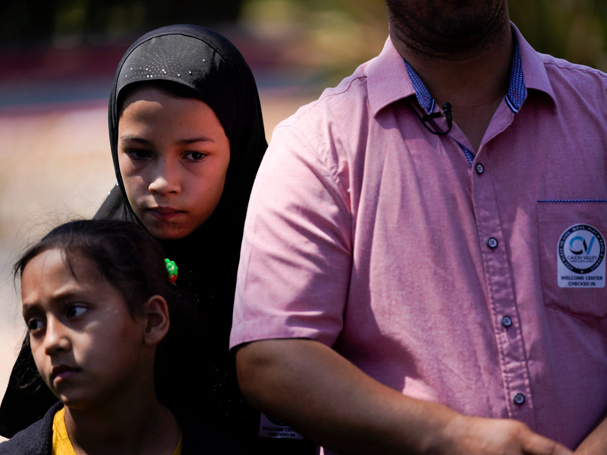 Palwasha Faizi, 10, above left, stands behind her sister, Parwana Faizi, 7, and alongside her father, Mohammad Faizi, during a news conference Thursday, Sept. 2, 2021, in El Cajon, Calif. The family were visiting relatives in Afghanistan in August, and were forced to escape as the Taliban seized power. Several families who live in the San Diego suburb of El Cajon spoke to reporters Thursday for the first time since returning from Afghanistan, where they described their harrowing escape after the Taliban seized power.