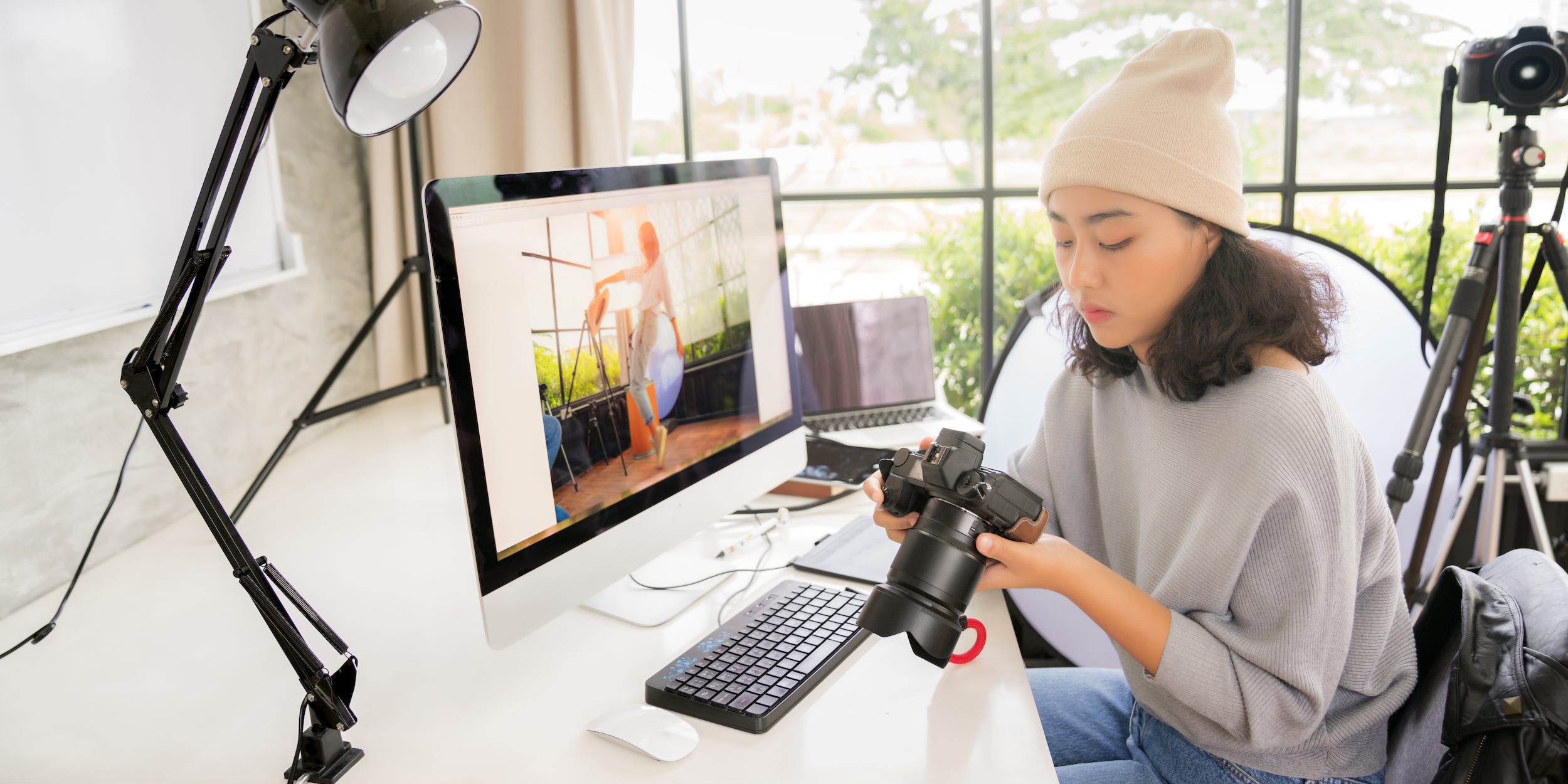 photographer editing photos on computer holding camera at desk