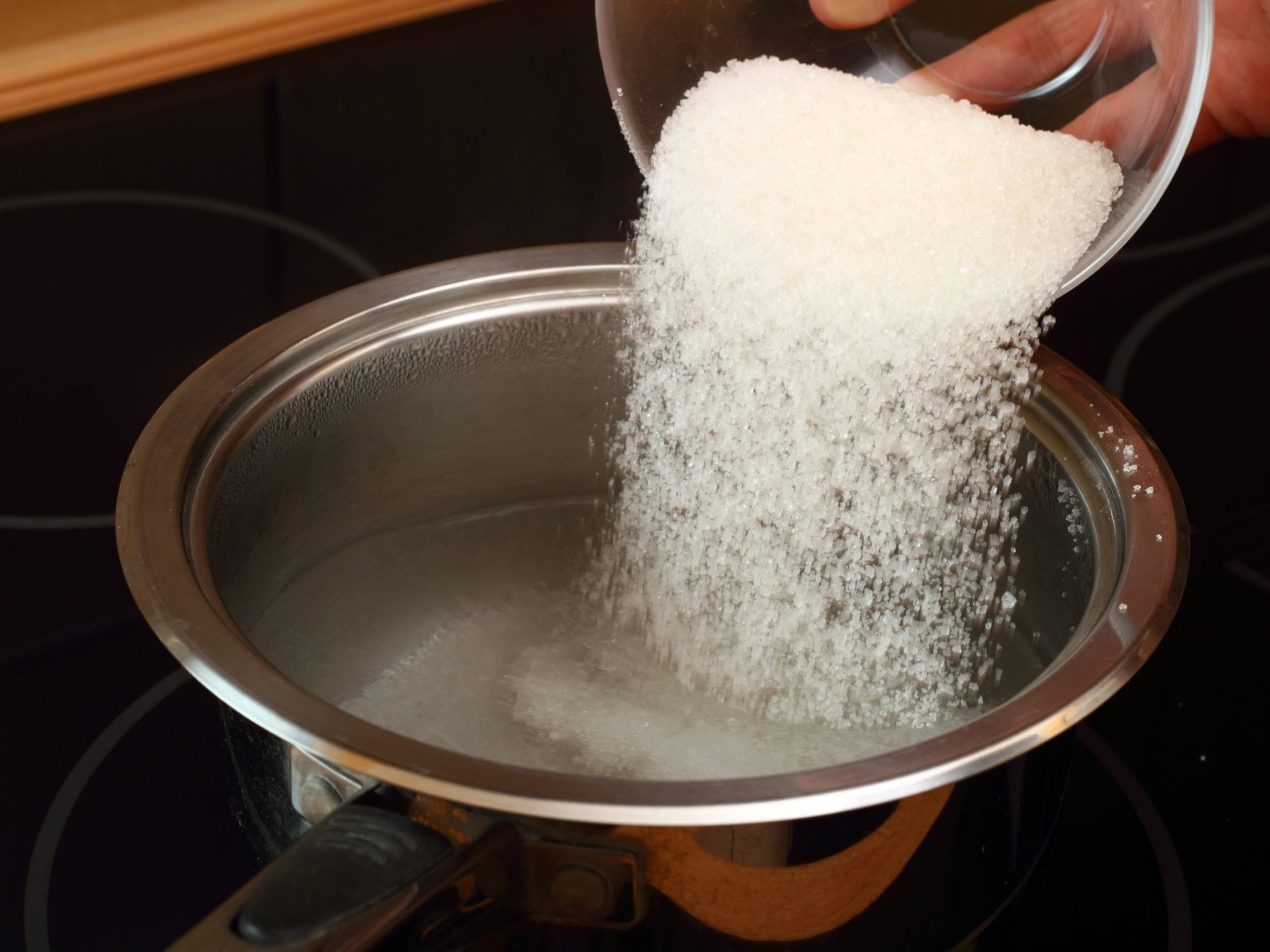 A hang pouring a bowl of sugar into a pot of water