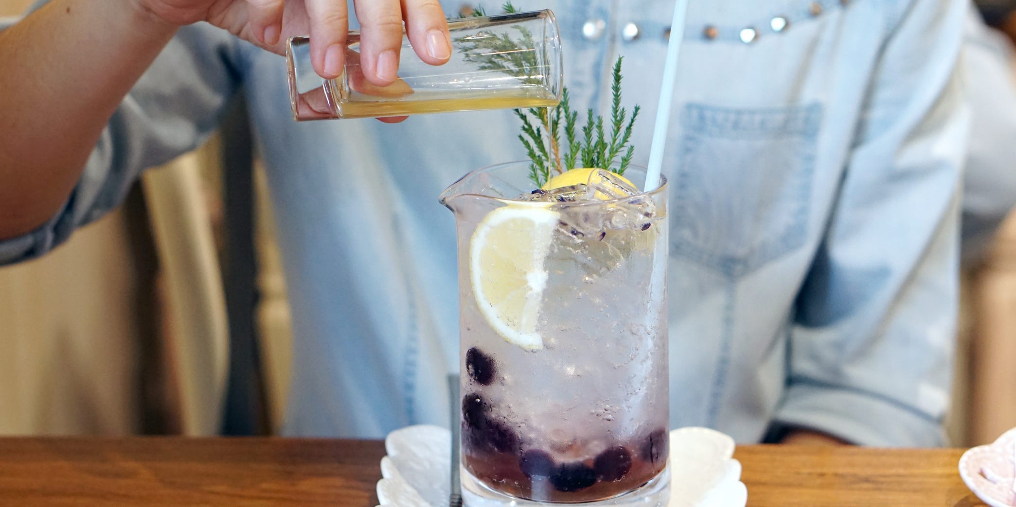 A hand pouring a shot glass of simple syrup into a cocktail