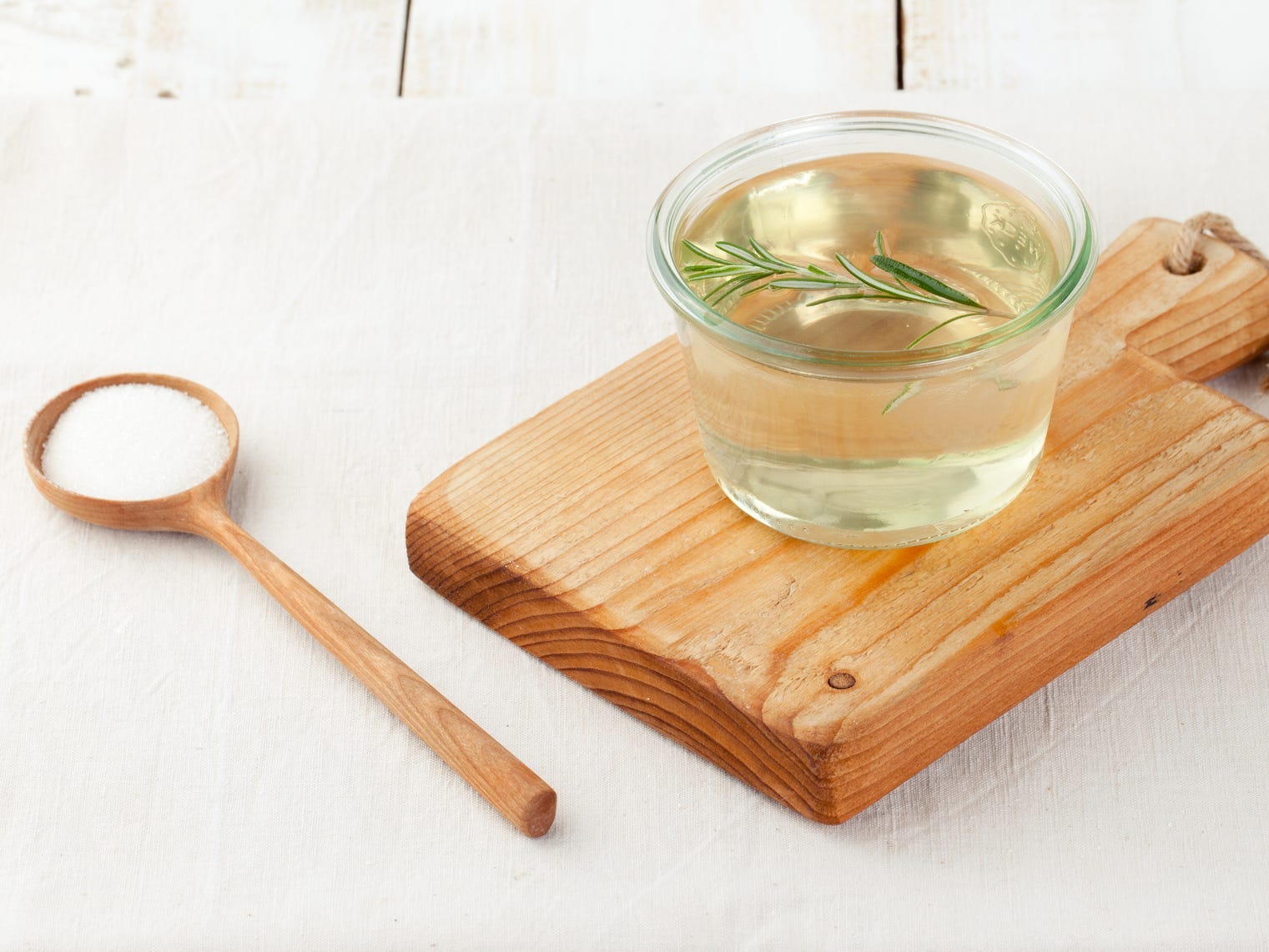 A glass jar of rosemary simple syrup sitting on a wooden cutting board