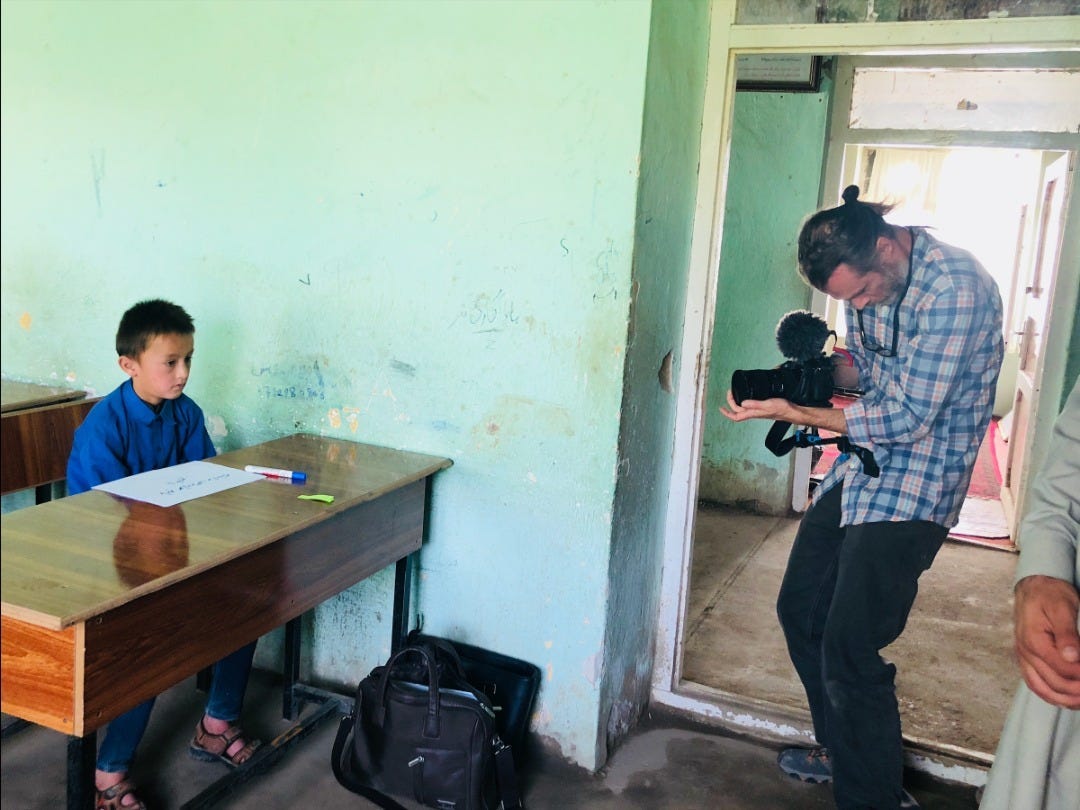 Nigel Walker holding up a video camera filming a young boy seated at a desk.