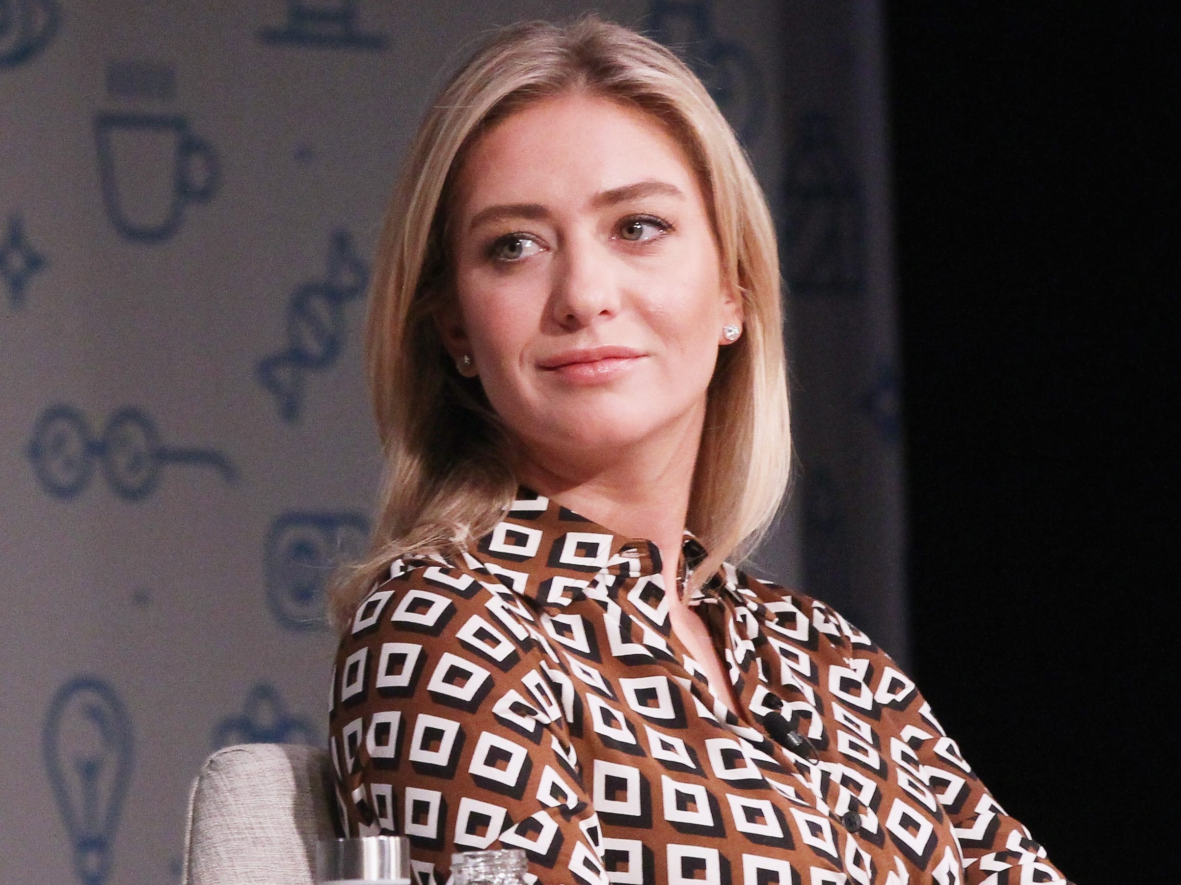 Whitney Wolfe Herd wears a brown and white dress while sitting on stage.