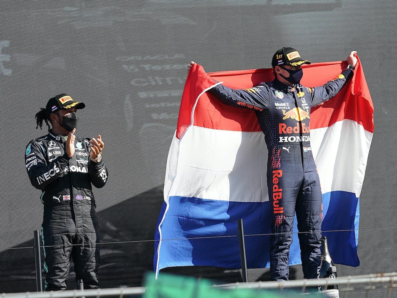 Max Verstappen celebrates on the podium with a Dutch flag while Hamilton looks on