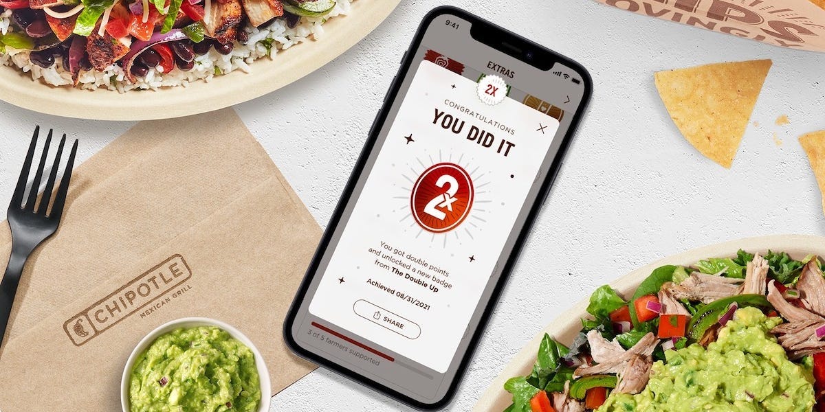 An iPhone displaying the Chipotle app. It's surrounded by Chipotle-branded items.