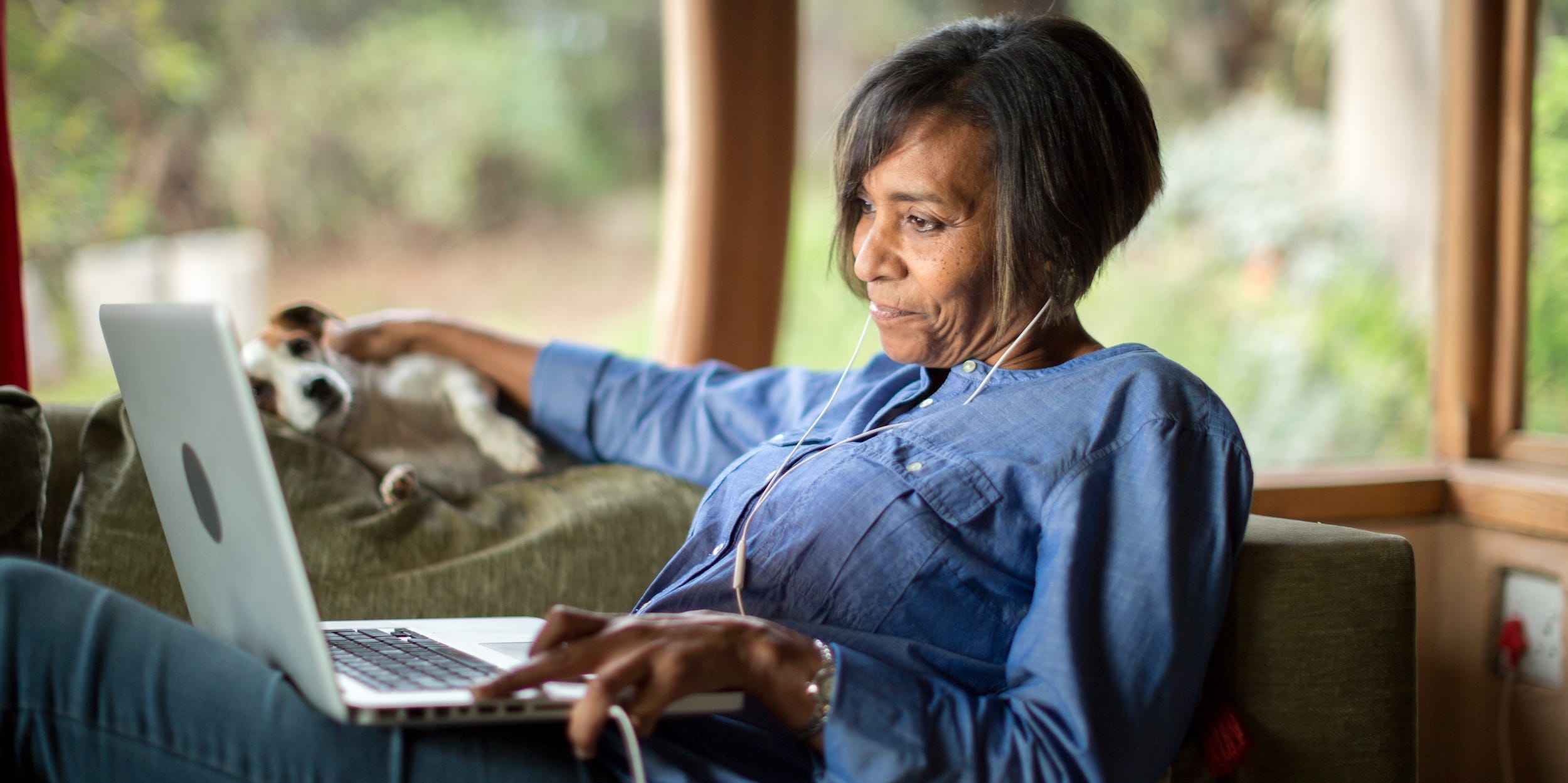 woman at home with dog looking at laptop on couch