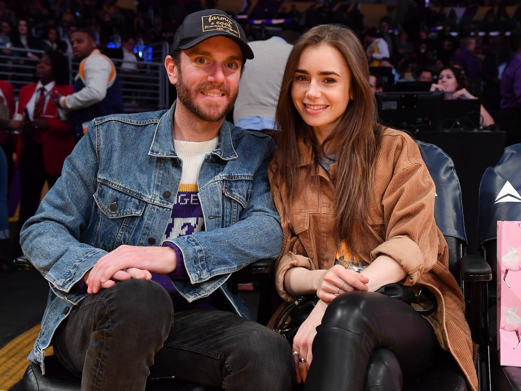 Charlie McDowell and Lily Collins smile at a basketball game.