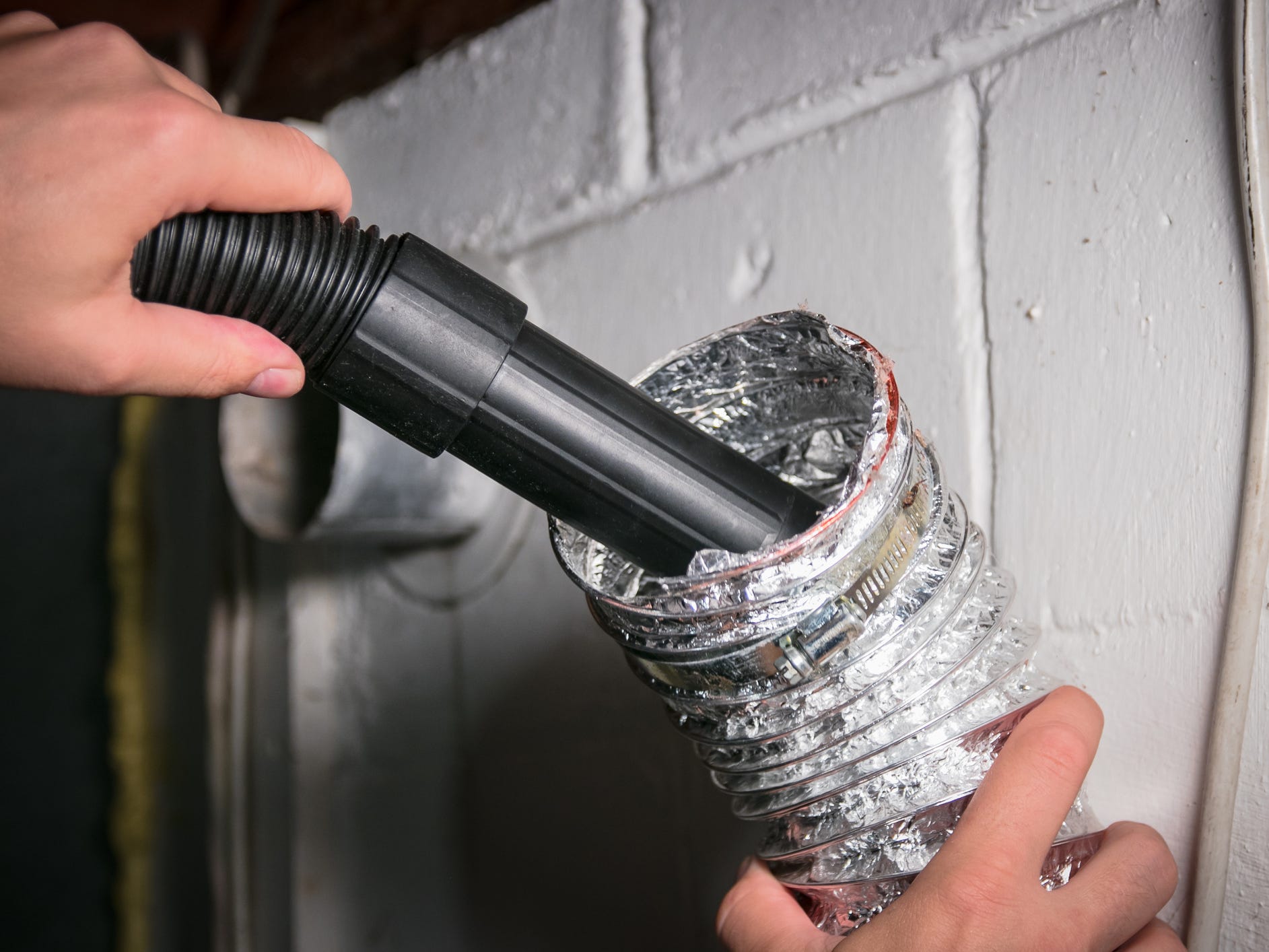 A person vacuuming the inside of a dryer vent duct