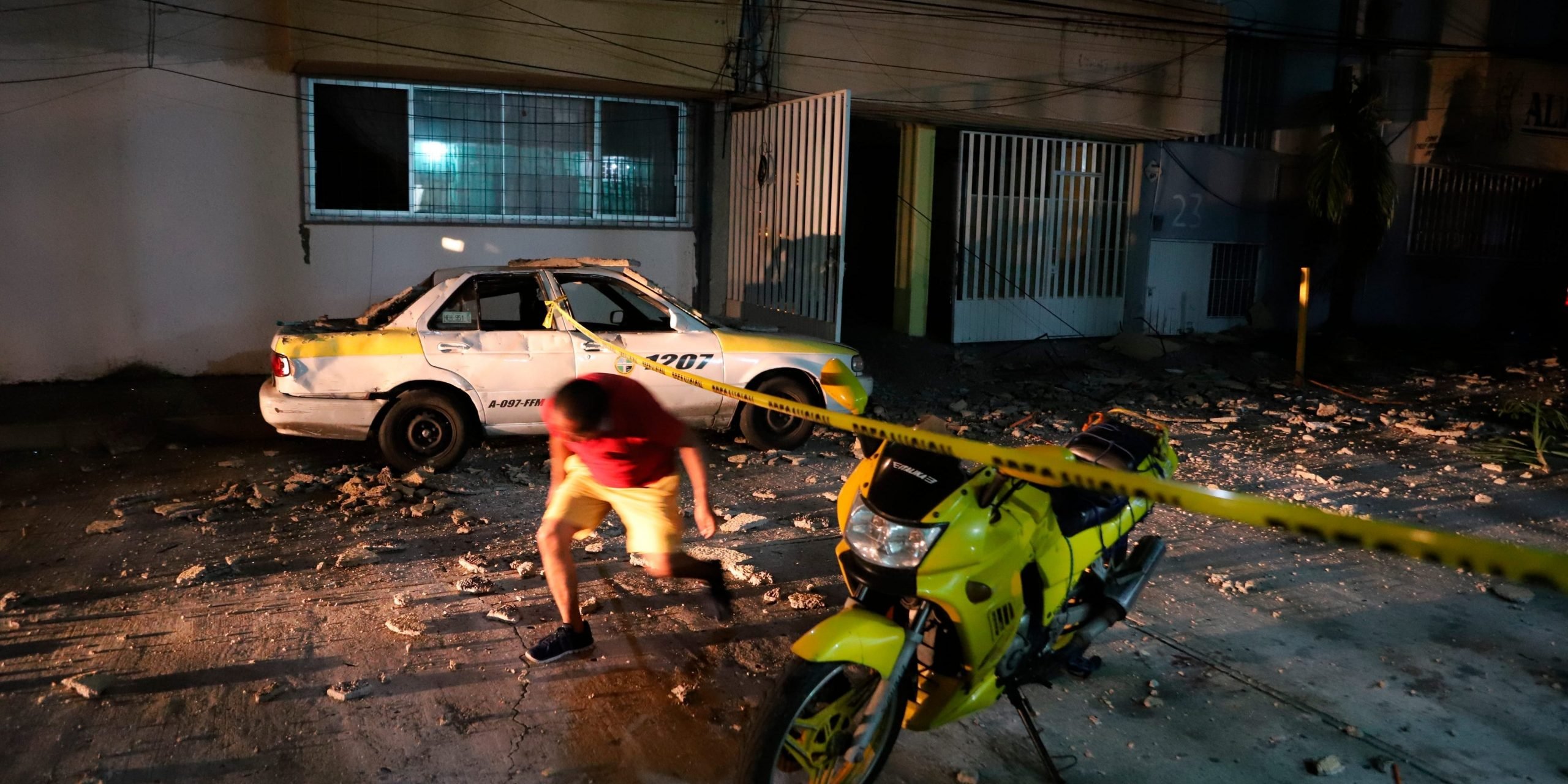 A man ducks under police tape, on a street covered with debris after a strong earthquake in Acapulco, Mexico, Tuesday, Sept. 7, 2021.