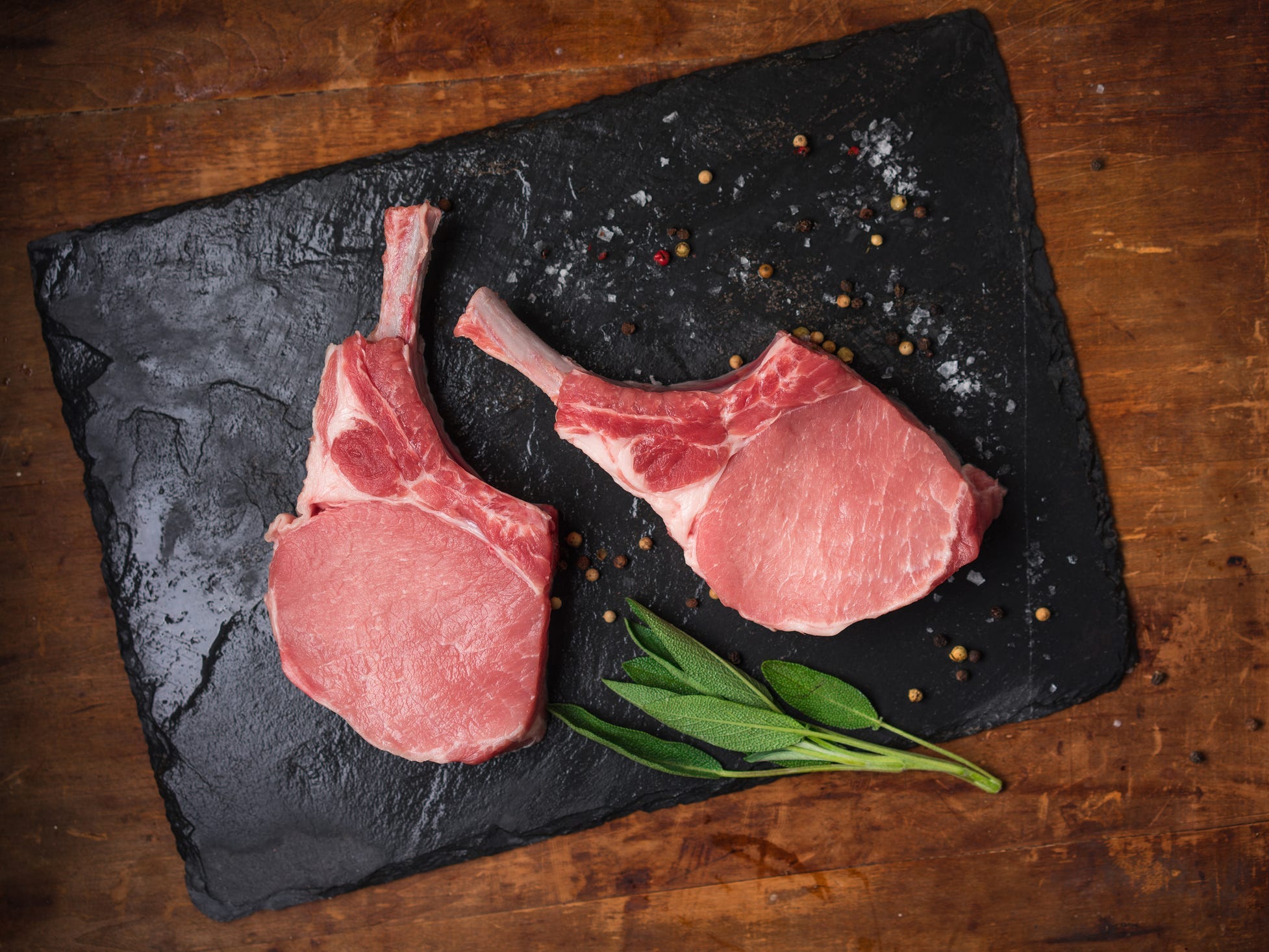 Two raw bone-in pork chops on a slate board