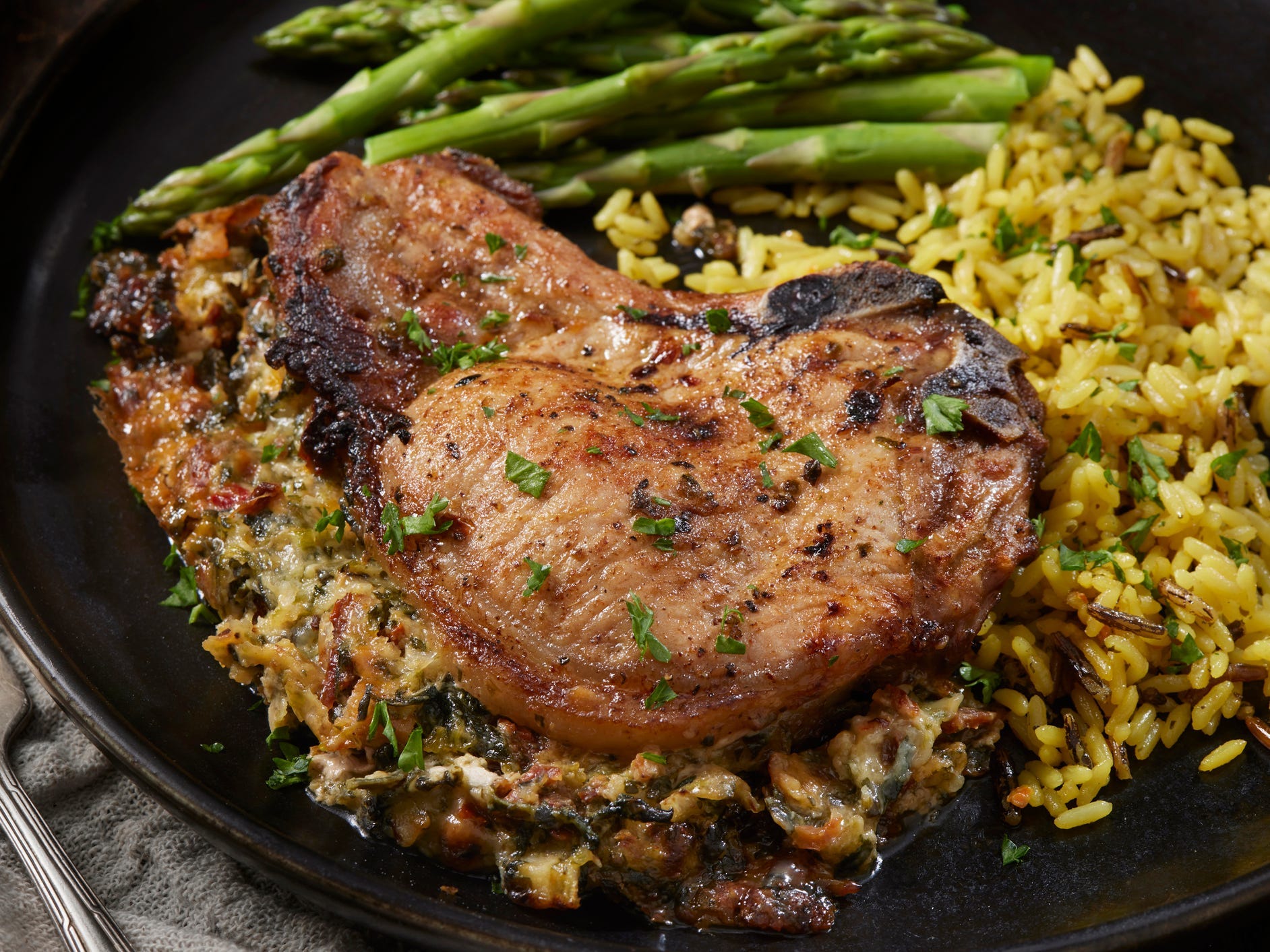 A pork chop on a bed of yellow rice with a side of asparagus