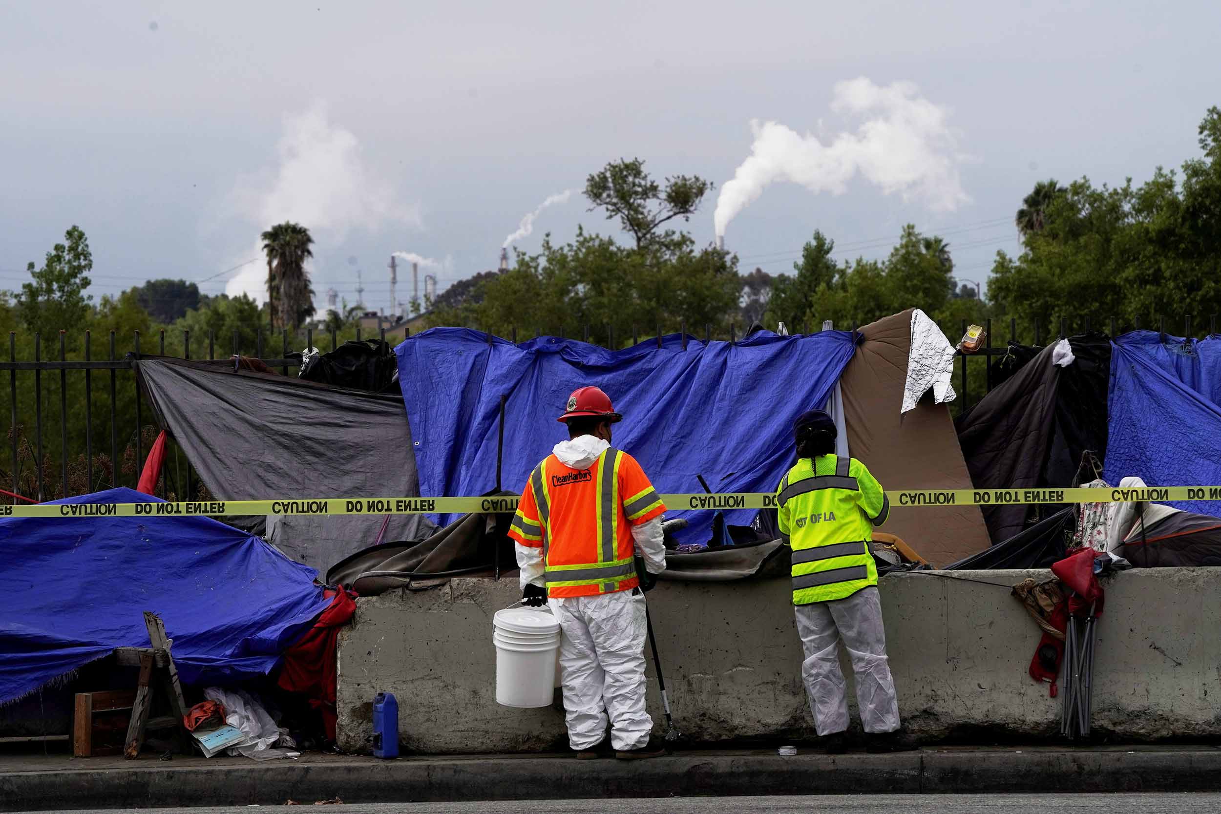 LA Sanitation & Environment (LASAN) workers observe a sidewalk dwelling as police and sanitation workers clear a homeless encampment in Harbor City, Los Angeles, California, U.S., July 1, 2021.