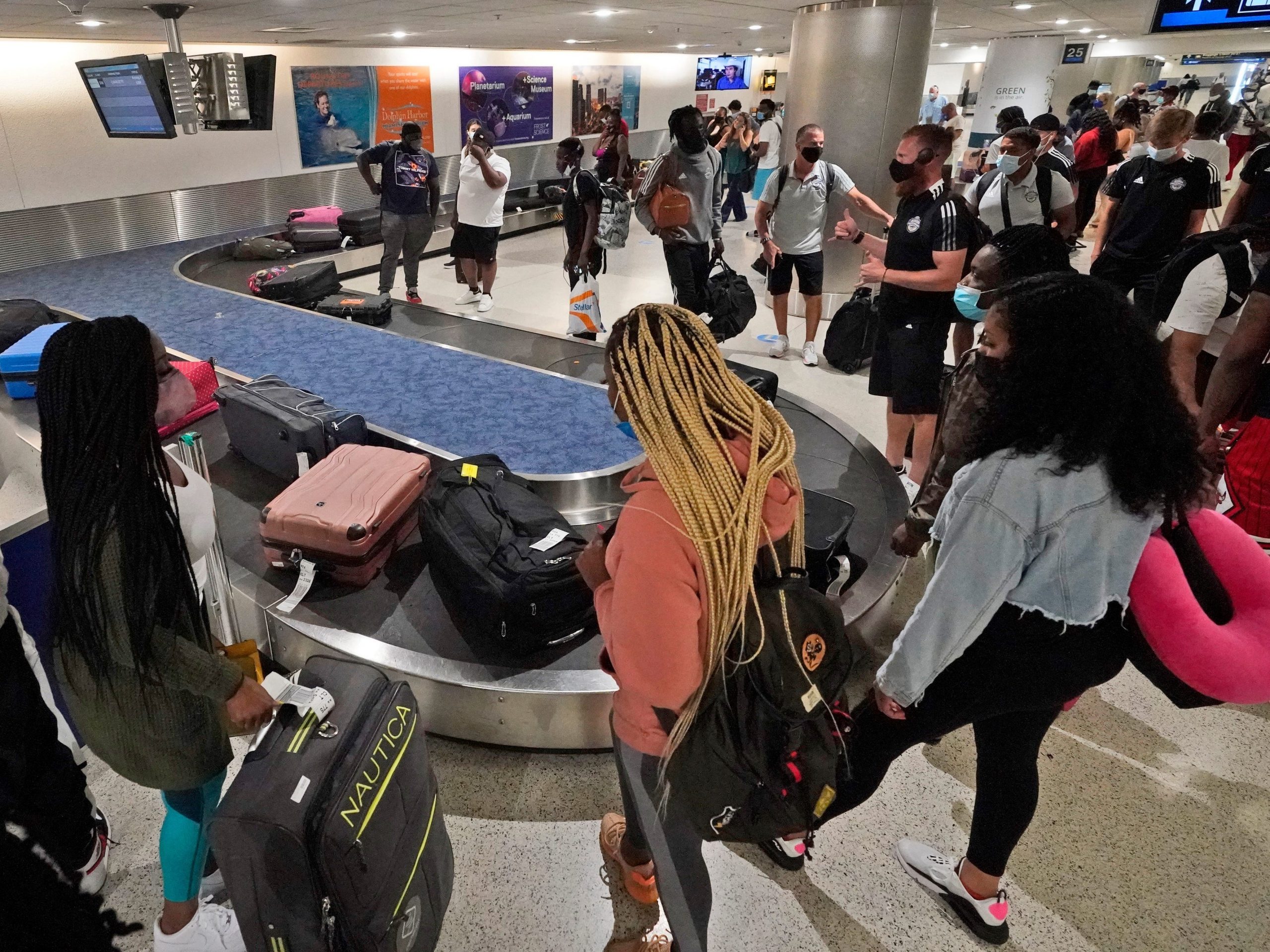 Travelers wait for their luggage at a baggage carousel, Friday, May 28, 2021, at Miami International Airport in Miami.