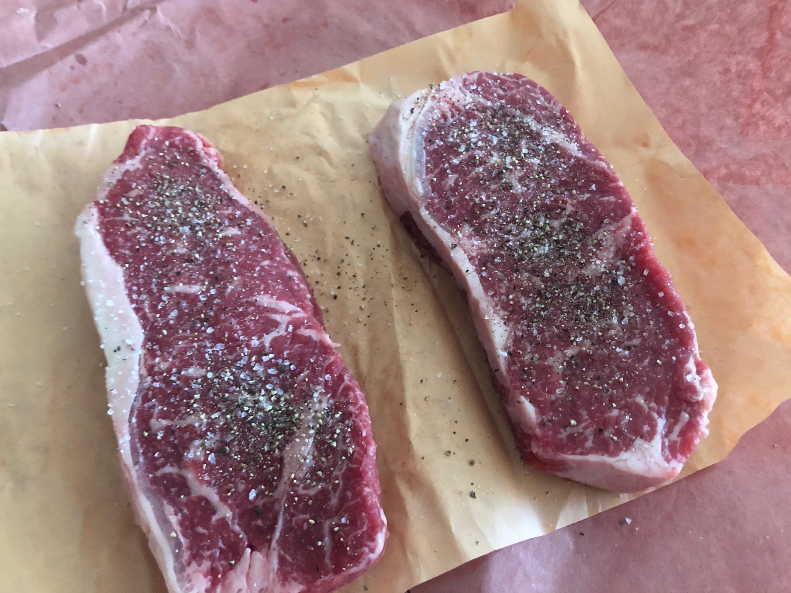 Two New York strip steaks with seasoning.