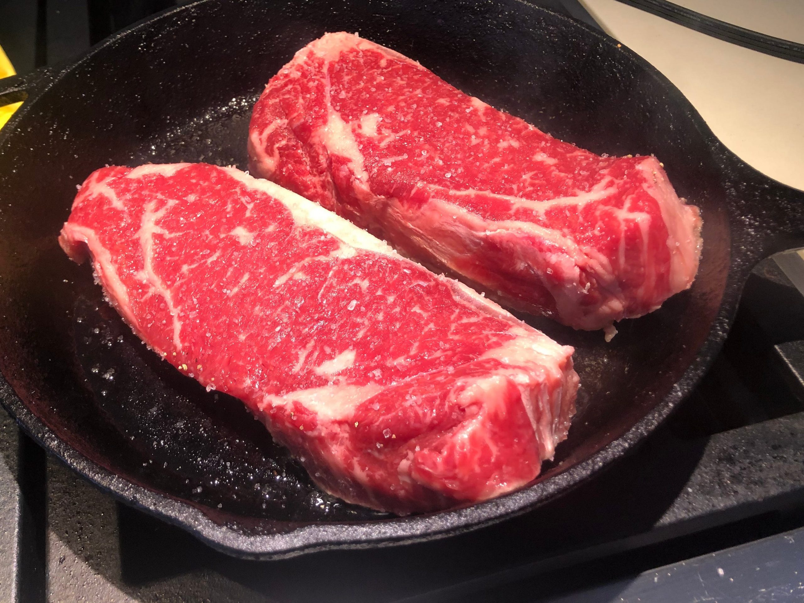 Two raw steaks on a cast-iron skillet.