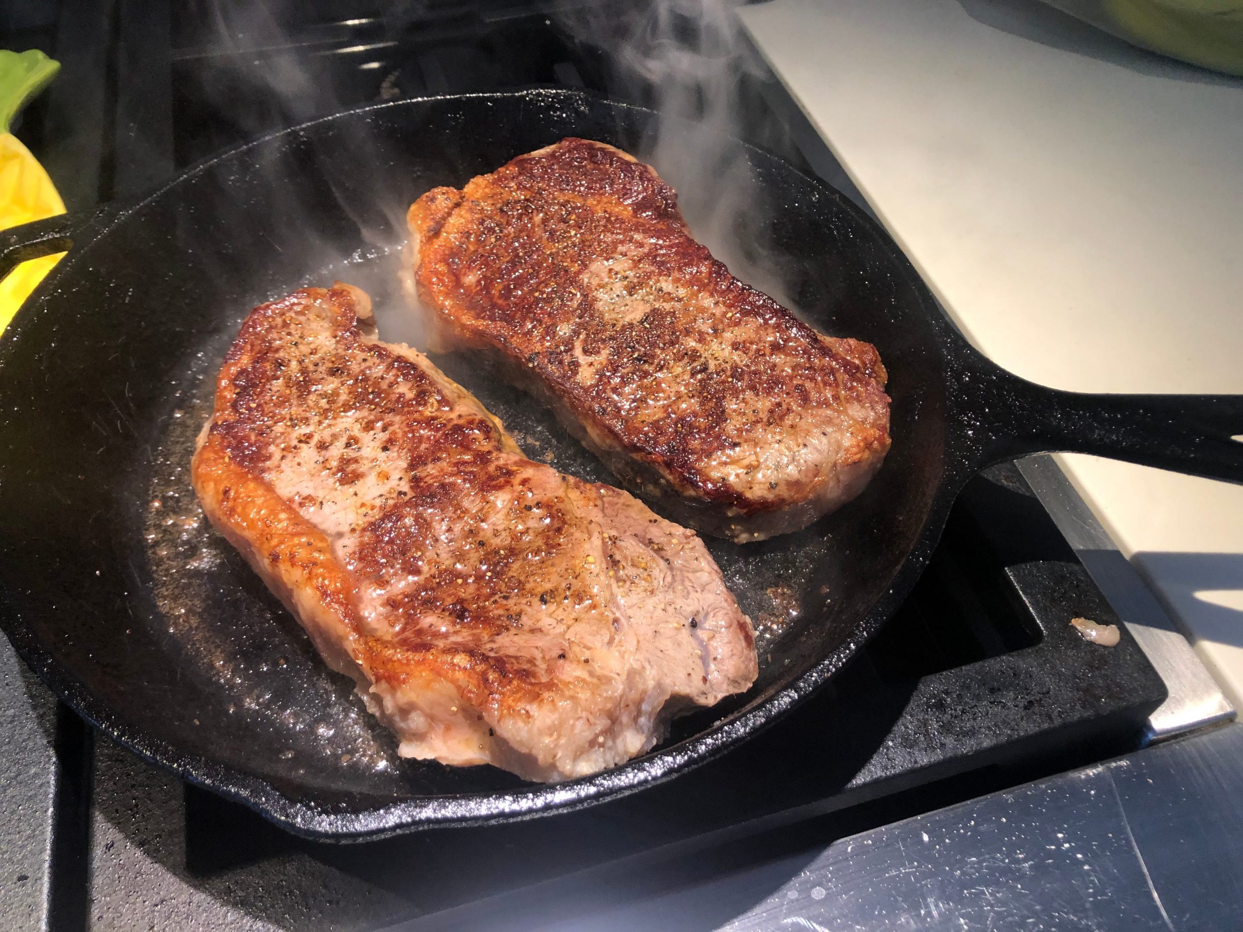 Two New York strip steaks on a cast-iron skillet.