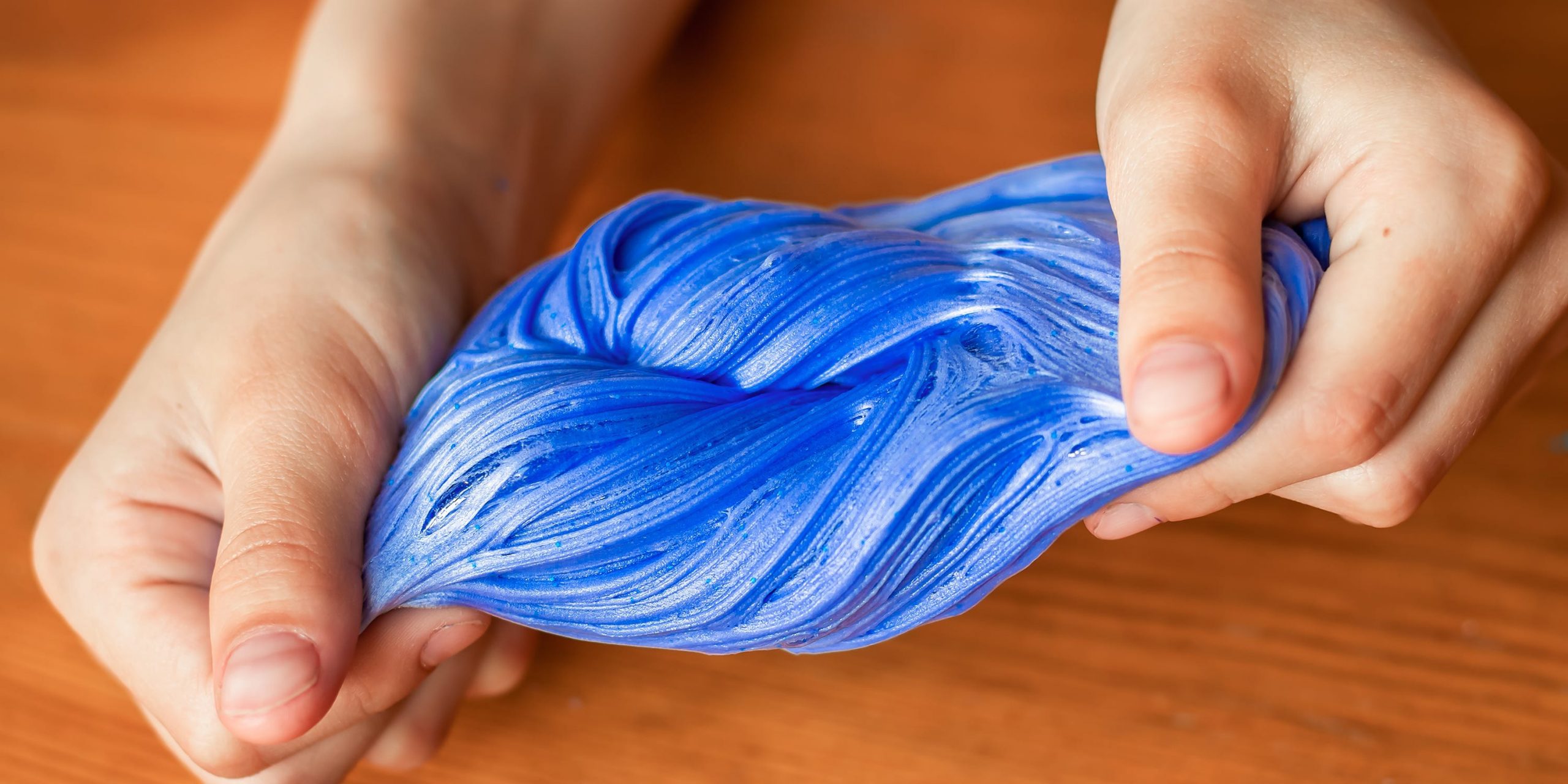 A closeup of a child's hands stretching blue slime