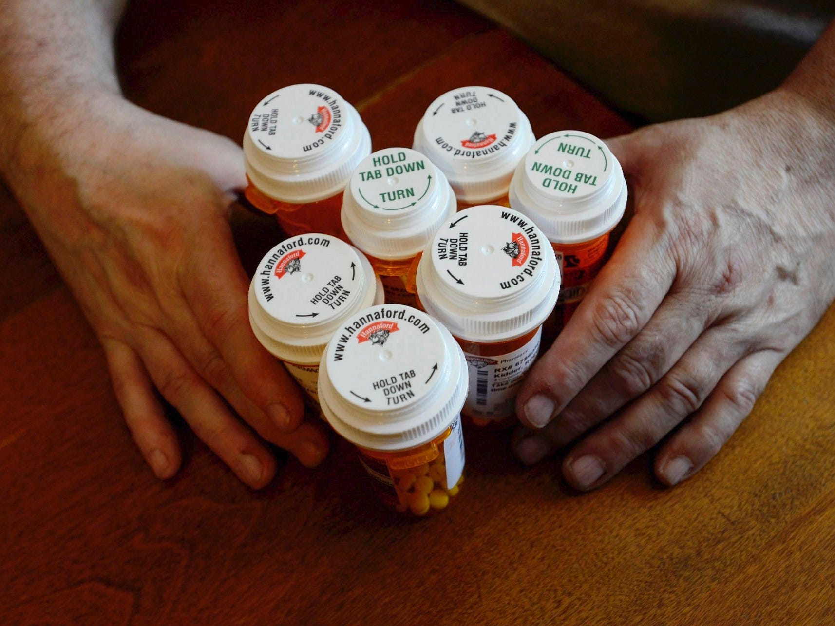 Two hands around six bottles of cholesterol medication on a table