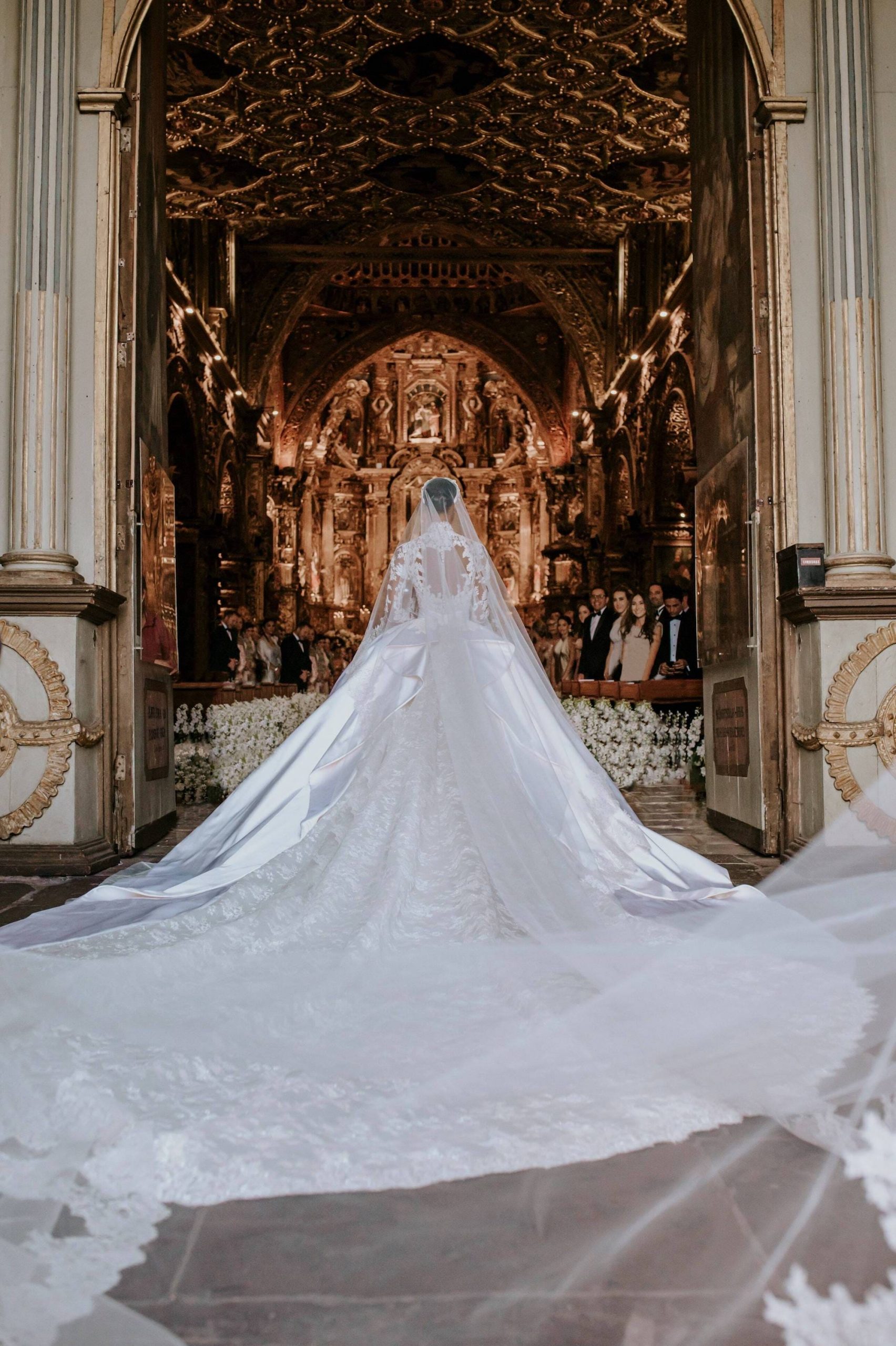 A bride walks into a church as her long train spreads out behind her.