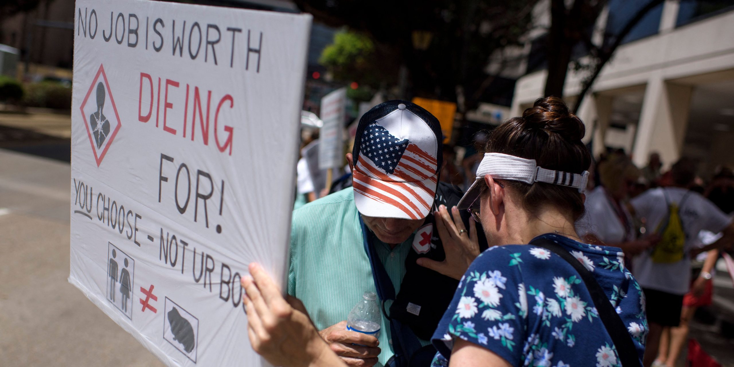 A woman holding a sign that says "no job is worth dieing for!" stands close to a man