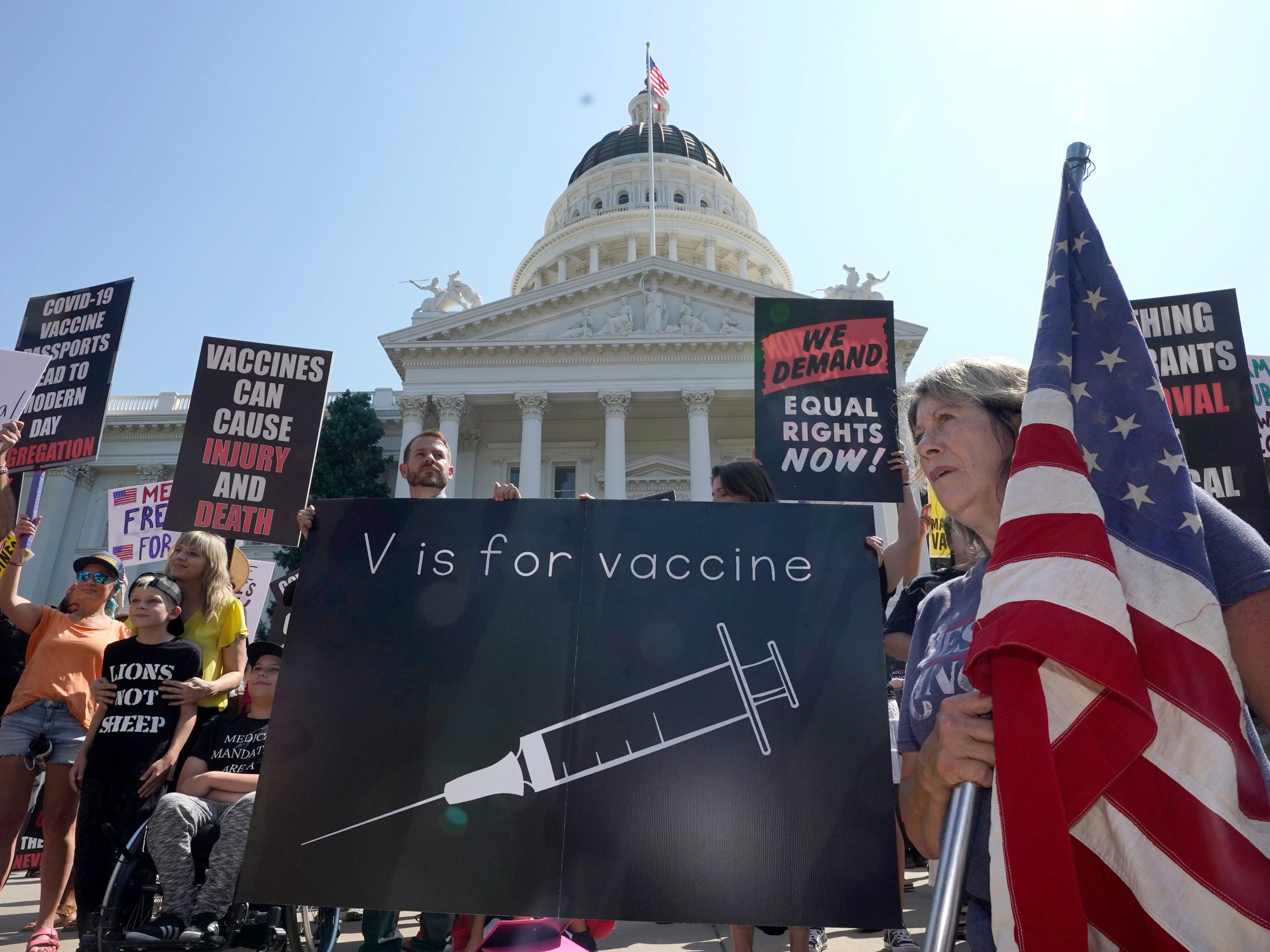 Protesters opposing vaccine mandates gather with signs and flags in front of the Capitol.