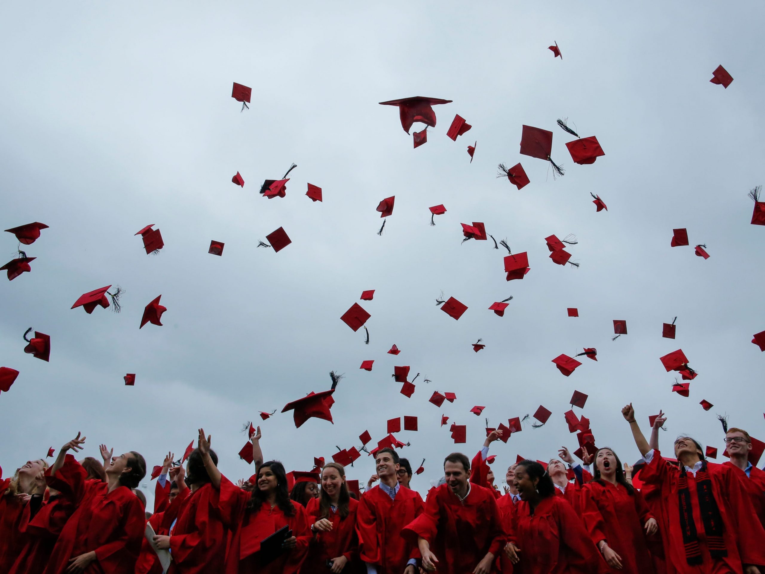 Hundreds of graduation hats are seen in the air above a crowd of students in graduation garb.