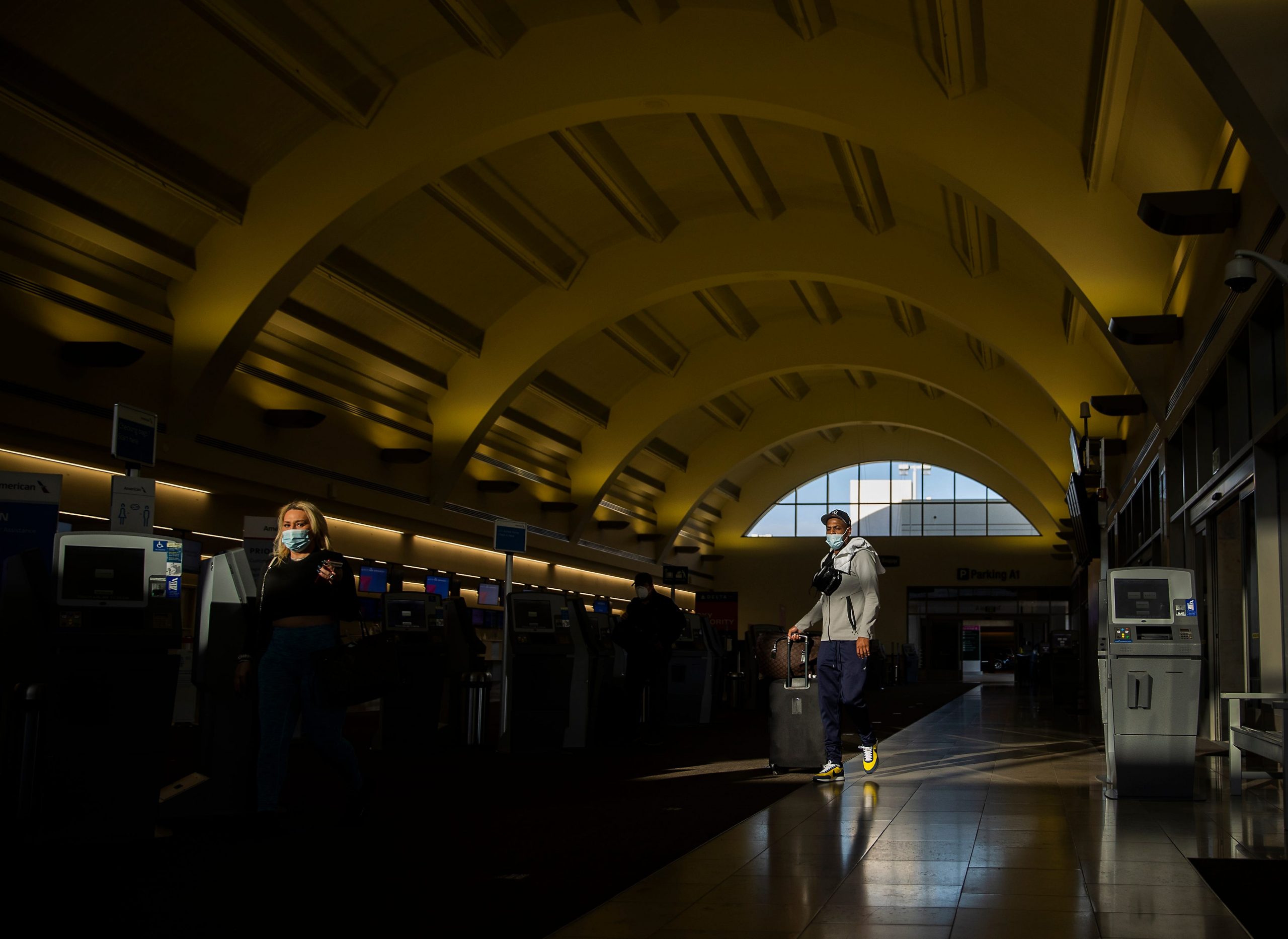A man in a mask stands under the curved terminal ceiling at John Wayne Airport in California